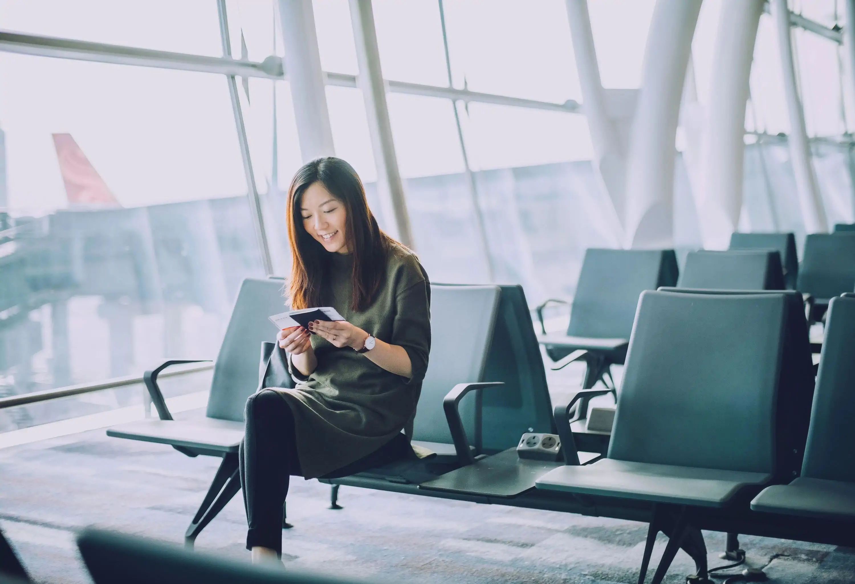 Young Asian woman holding passport and boarding pass on hand waiting in the departure lounge in airport