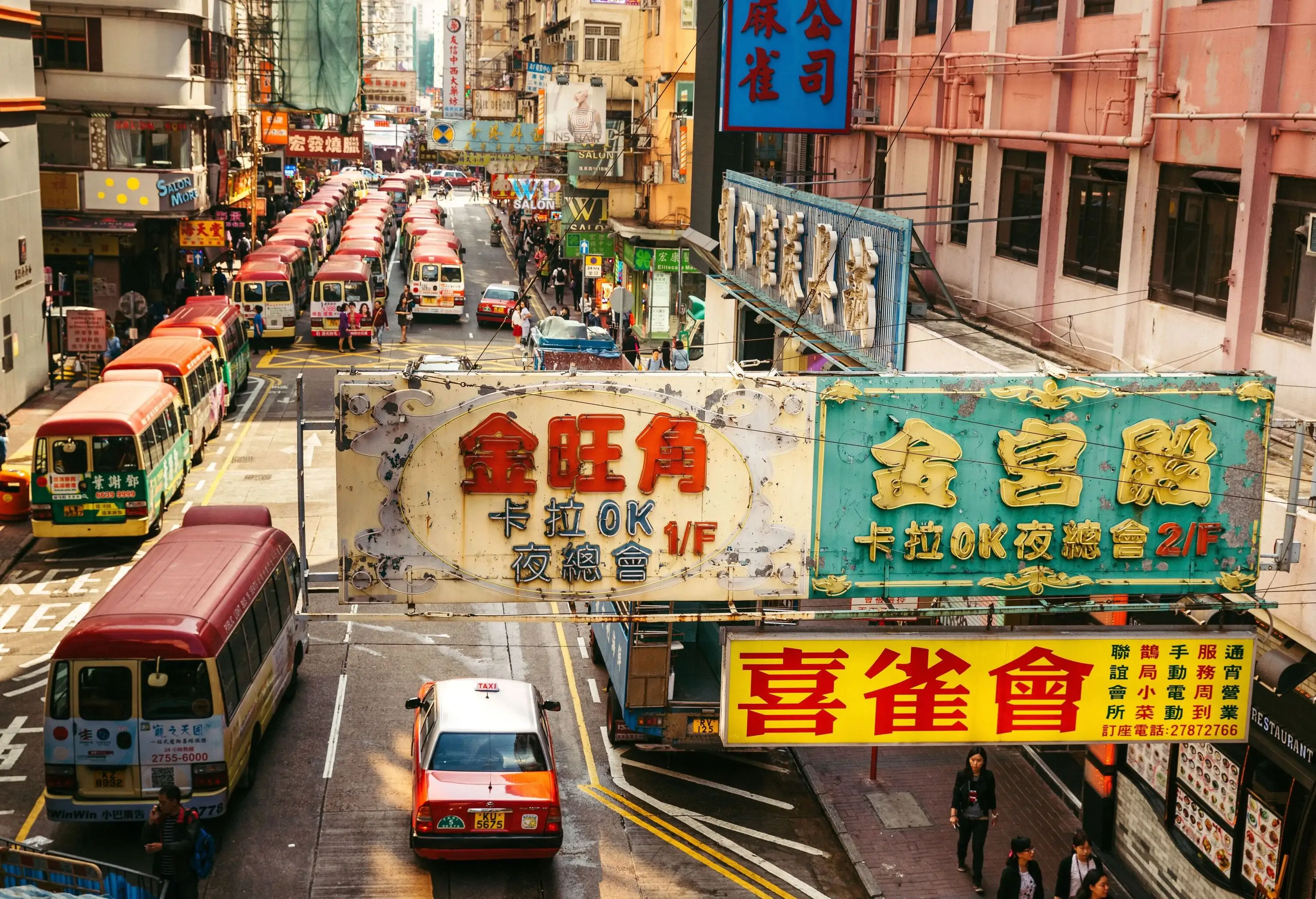 Busy street with advertising signs and buses in Kowloon Peninsula district in Hong Kong. The City is known worldwide for its colorful signs. Pedestrians walking along the busy road with many shops.