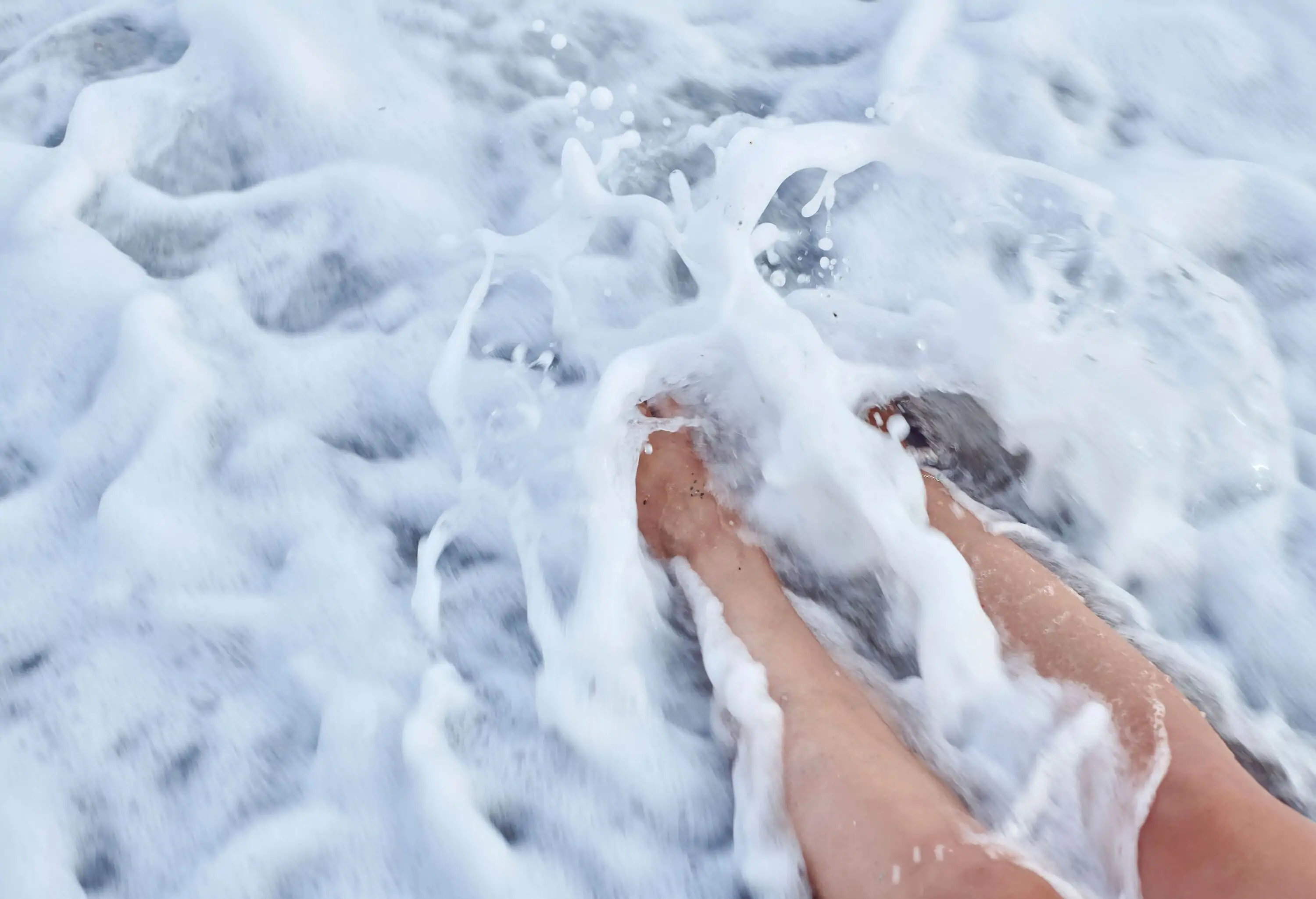 A set of legs immersed in a beach's foaming waves.