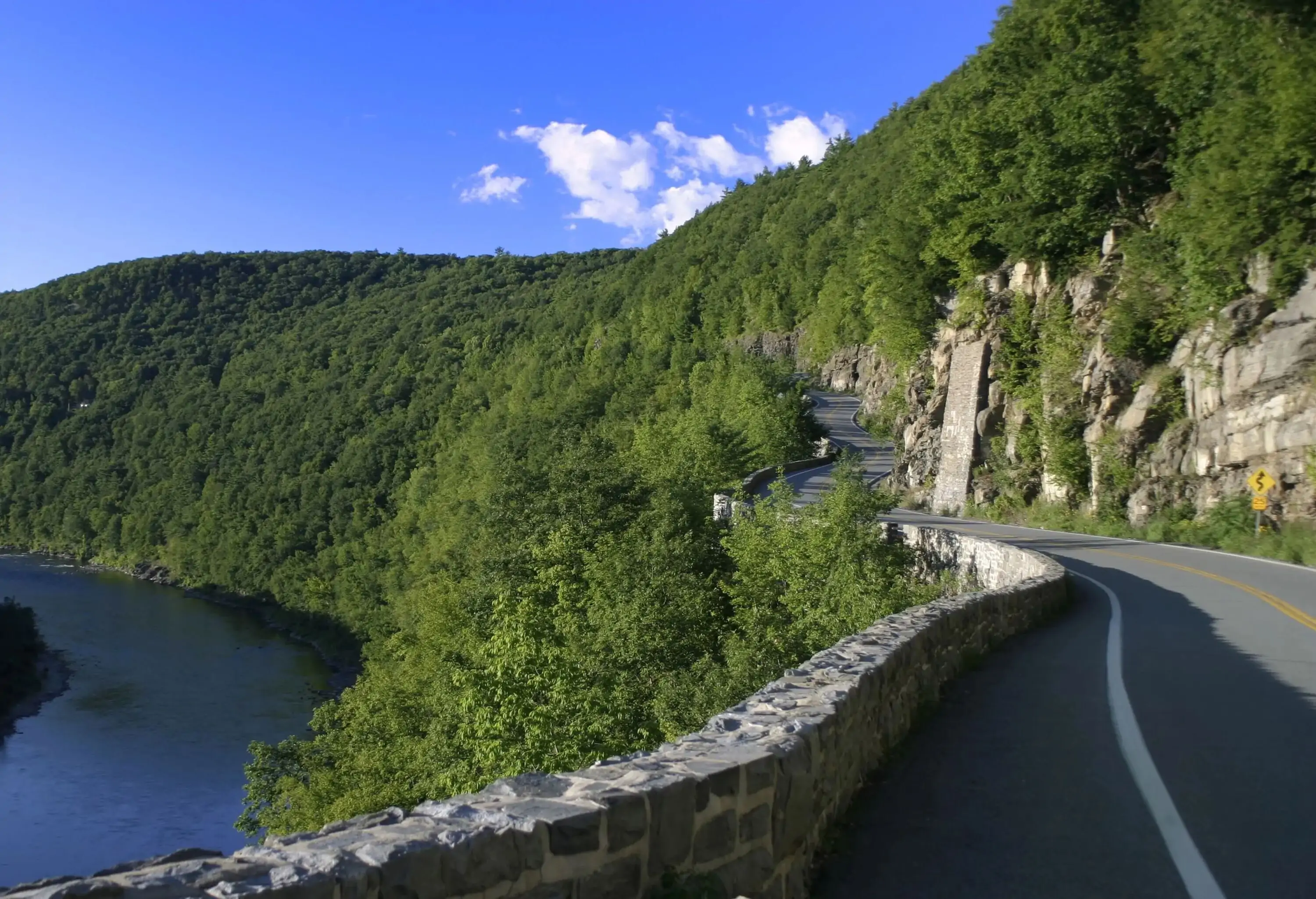 An empty road along a forested cliff with overlooking views of a calm river.