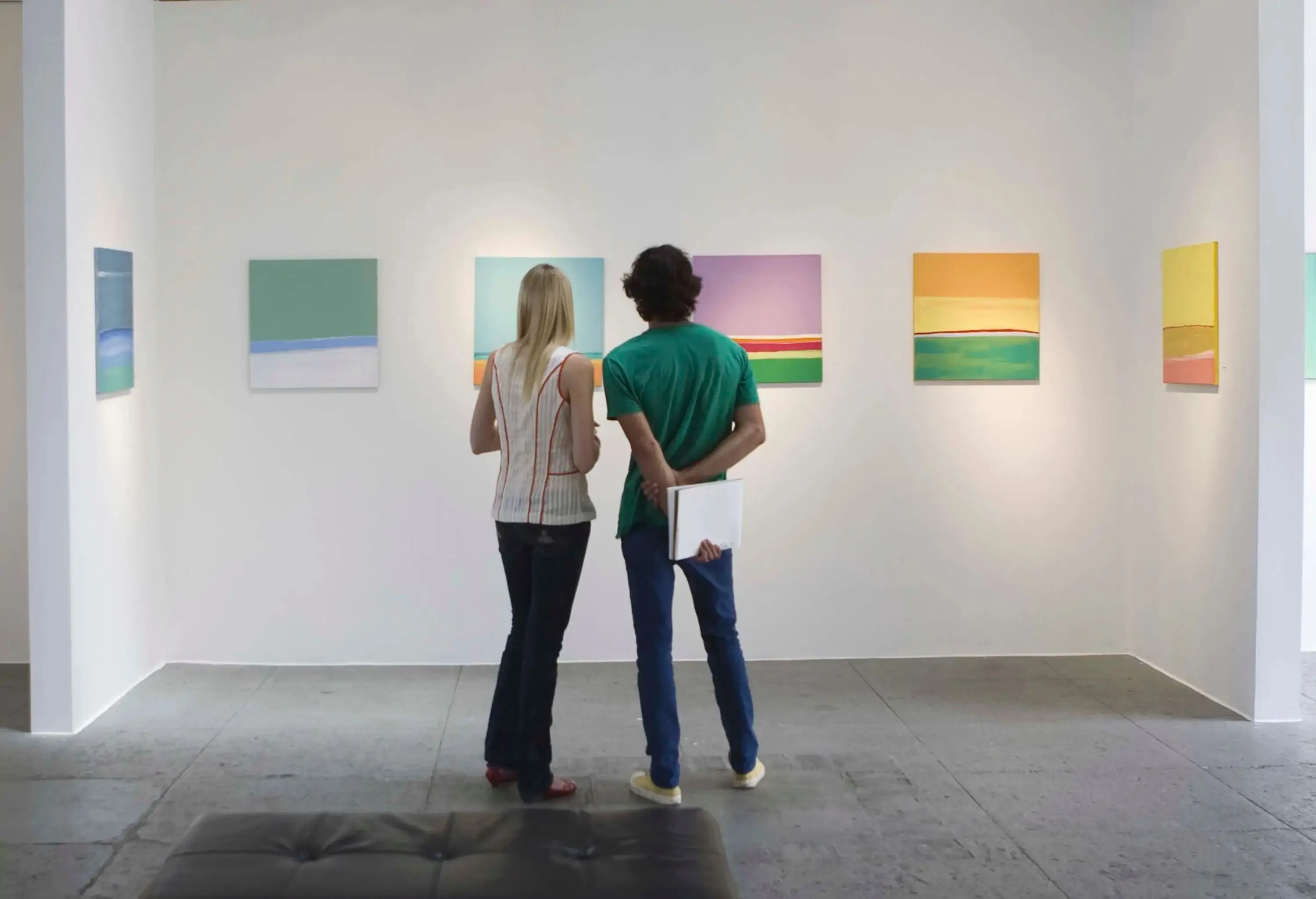 A male and a female friend are looking at the paintings in the museum.