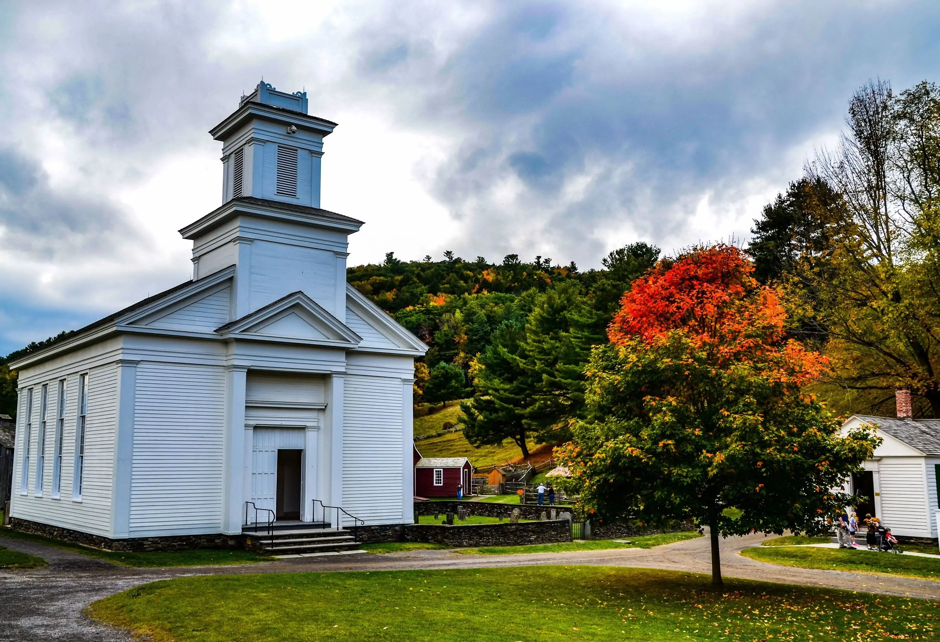 A white church in a rural village surrounded by vibrant autumn foliage.