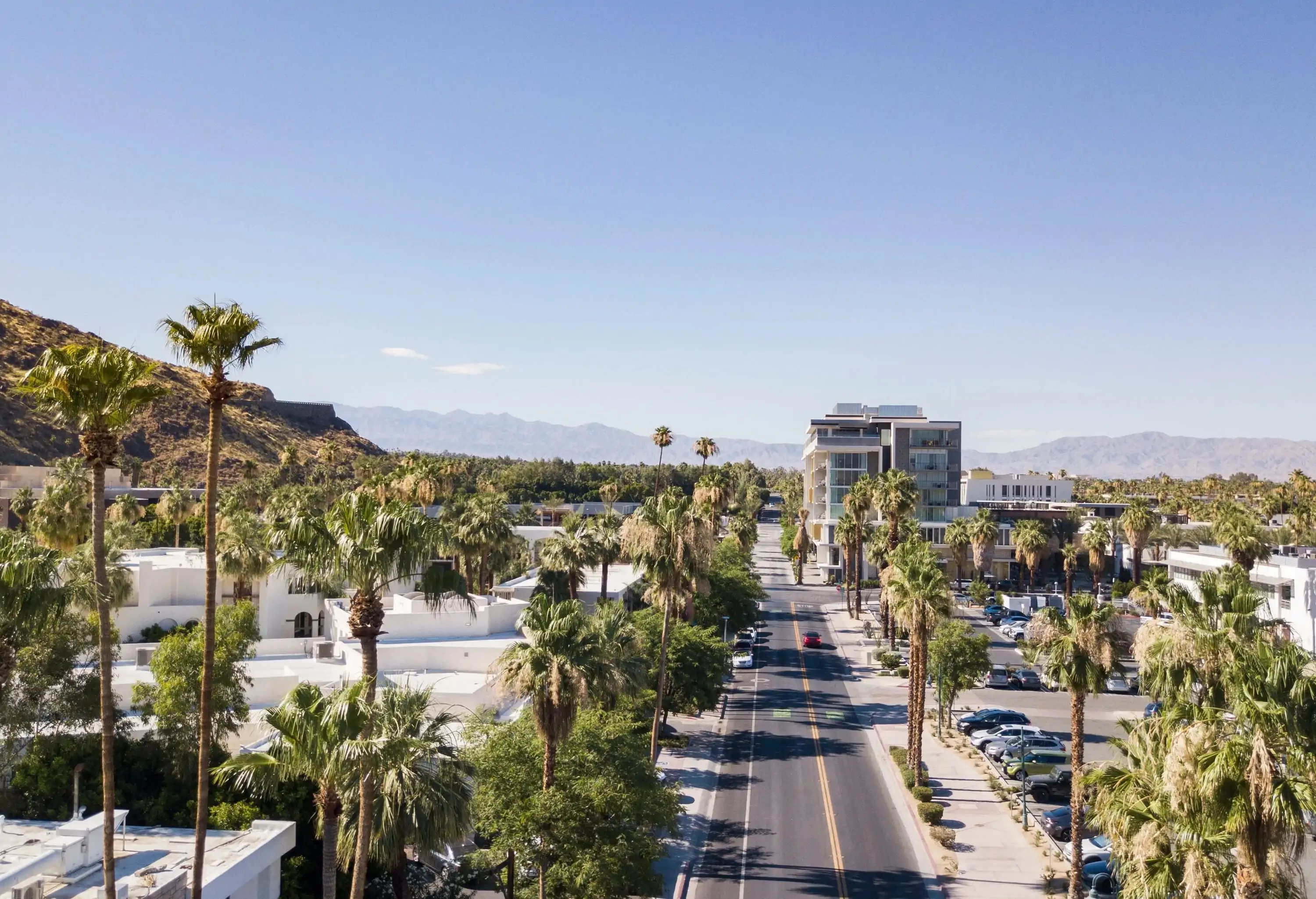 A tree-lined road across a parking lot and a cluster of residences in a city. Palm Springs, California