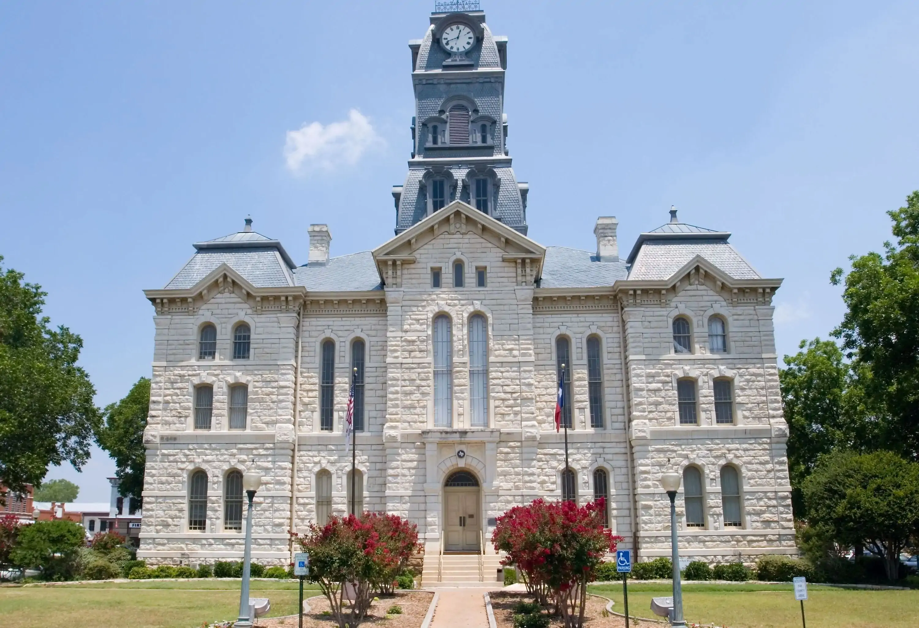 An old three-storey limestone courthouse crowned with an imposing clock tower stands tall against the clear blue sky.