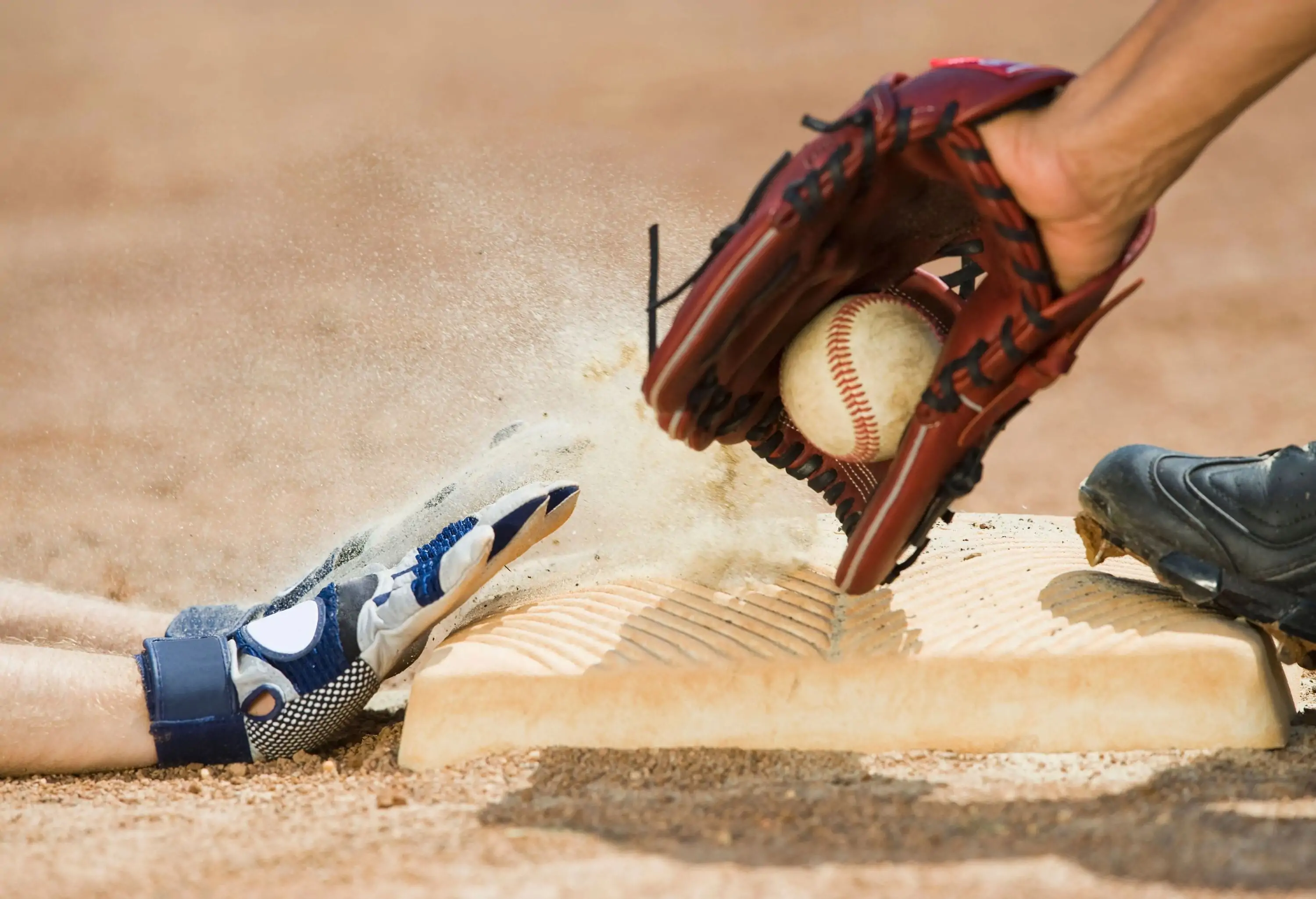 A gloved hand catches a baseball as another hand reaches out to touch a base.