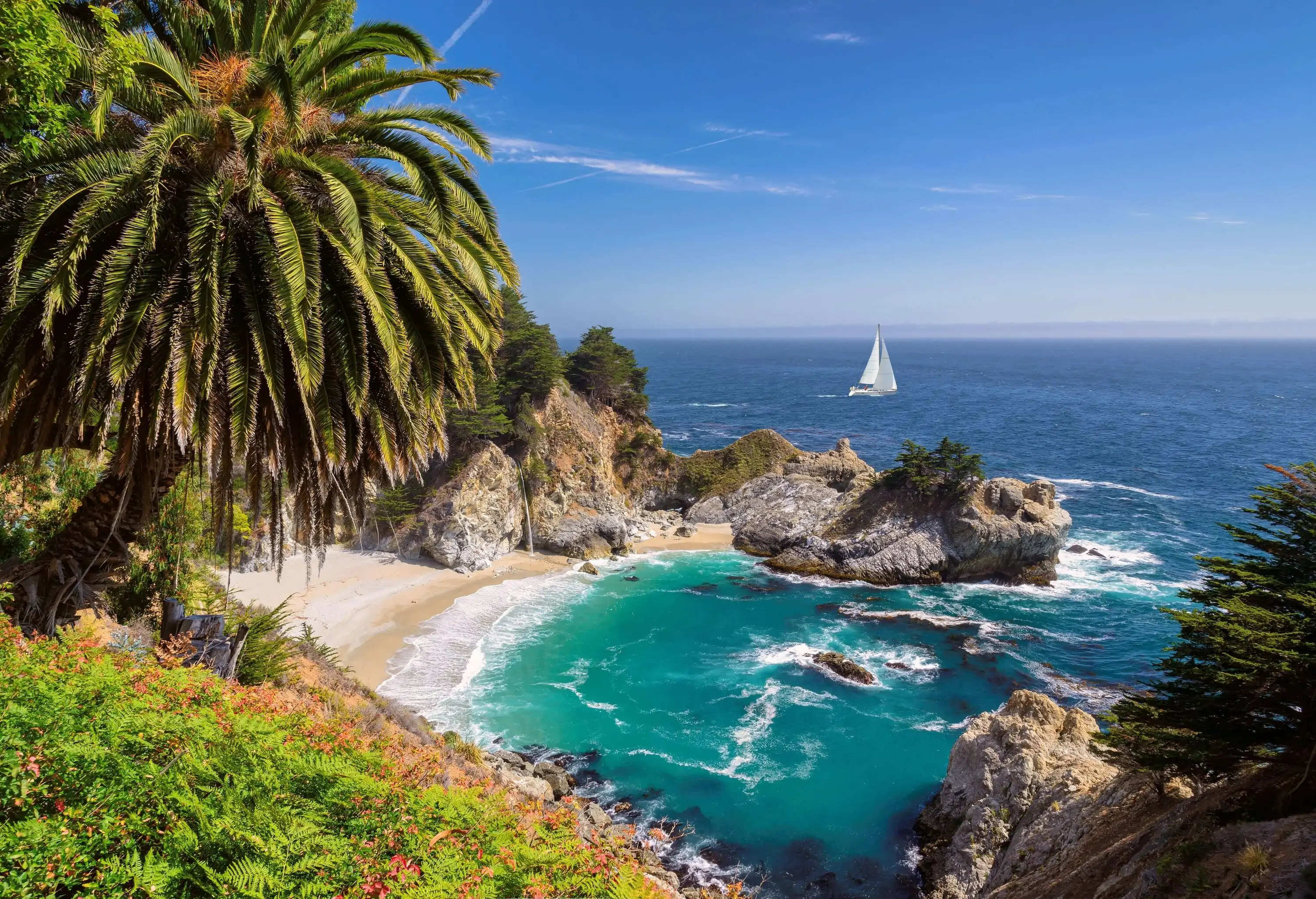 A sheltered cove with coastal rocks and distant views of a white yacht in the middle of the ocean.