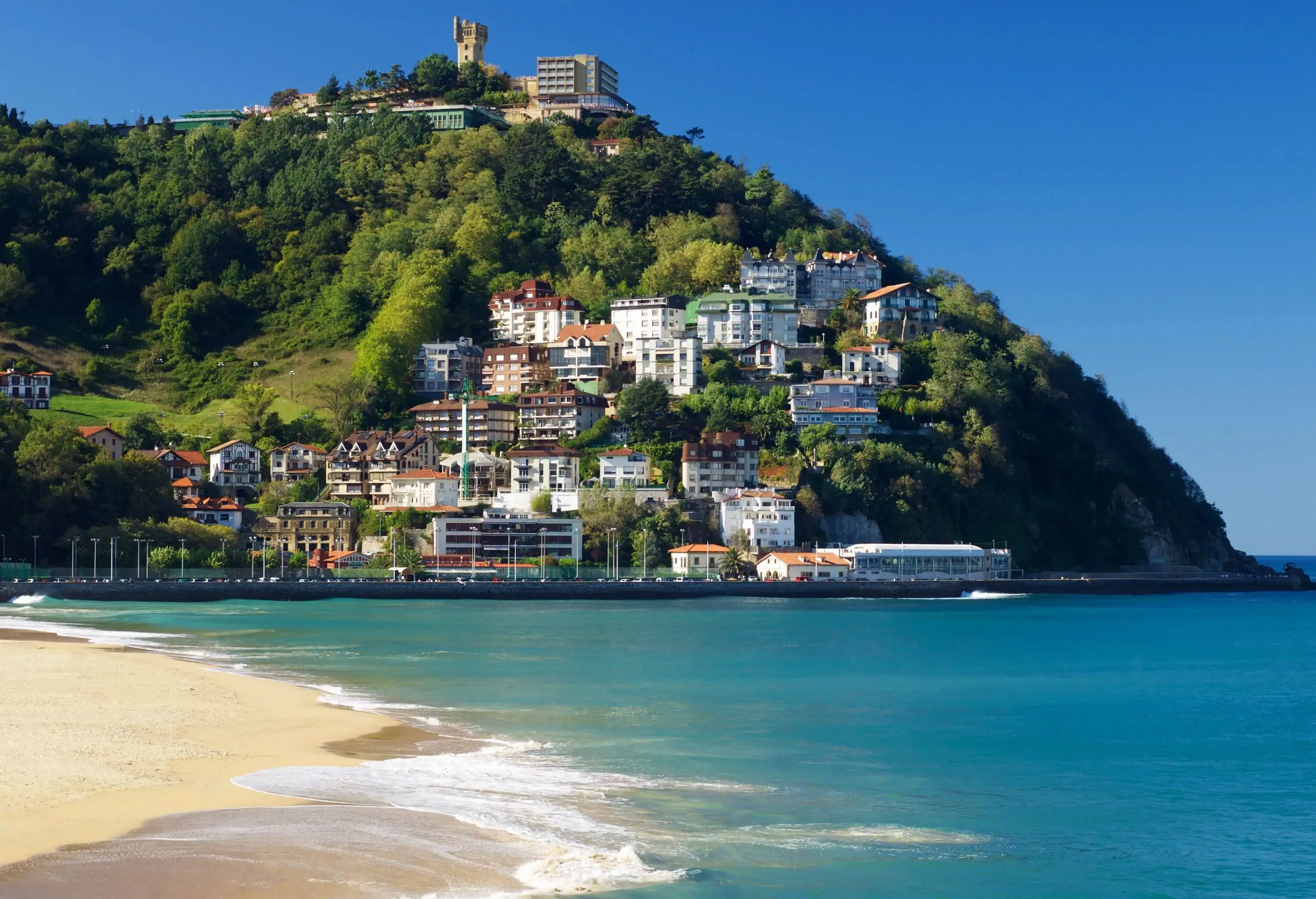 A neighbourhood built on a hill surrounded by trees near a beach.