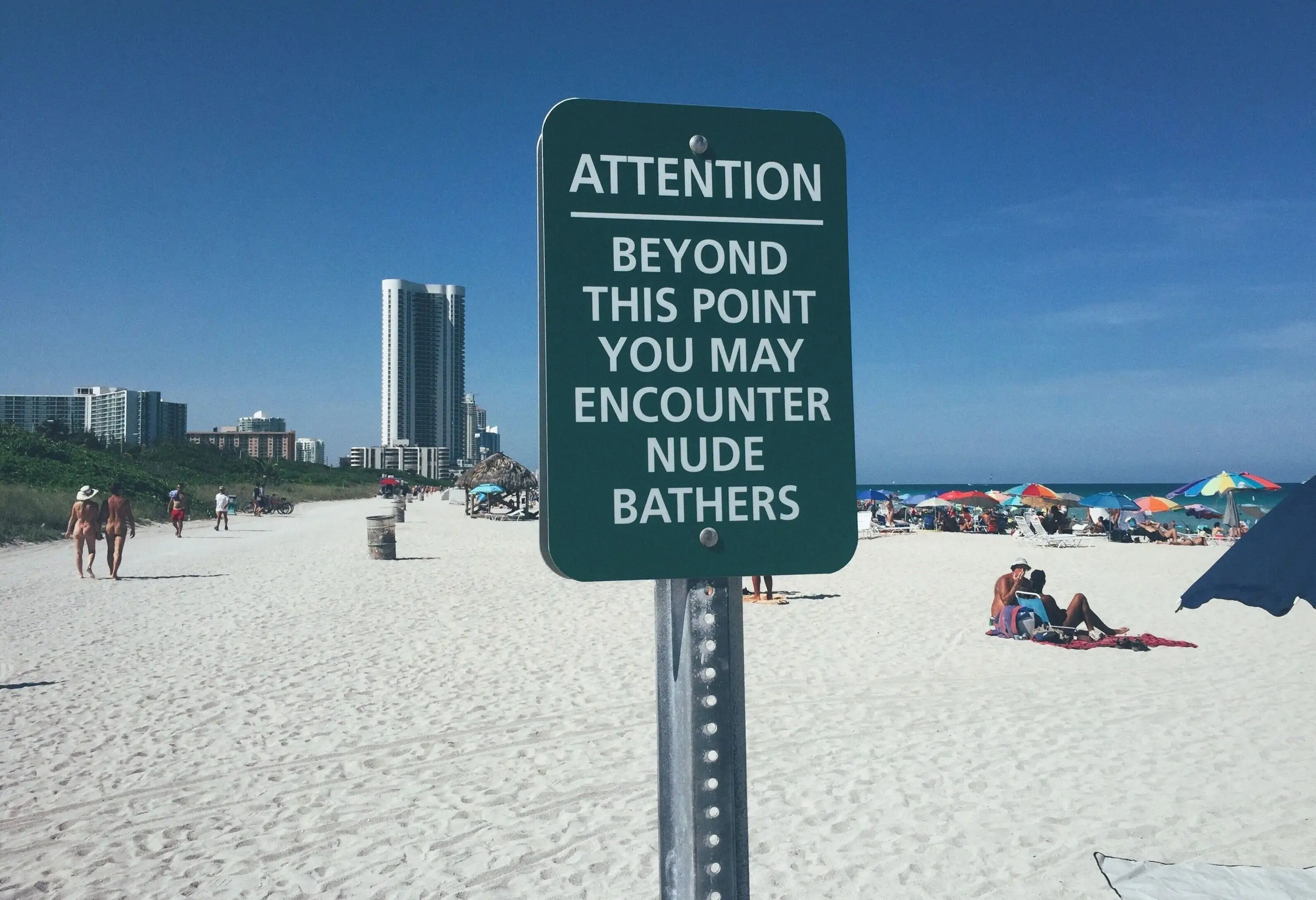 Many people are having fun on the fine white sand beach with a notice sign hung on a pole.
