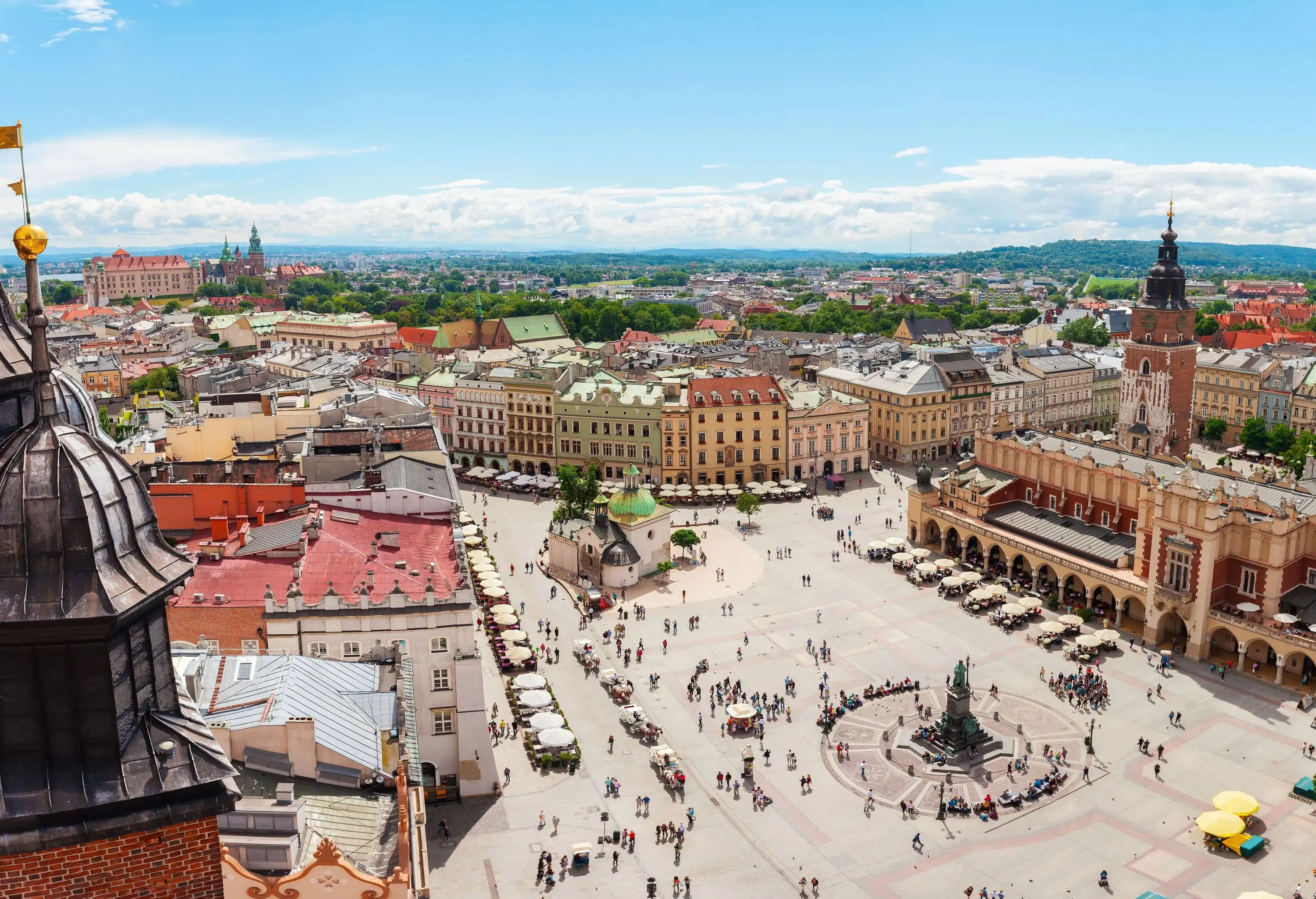 A crowded public square with tents, outdoor dining spots, and a central statue surrounded by city buildings.