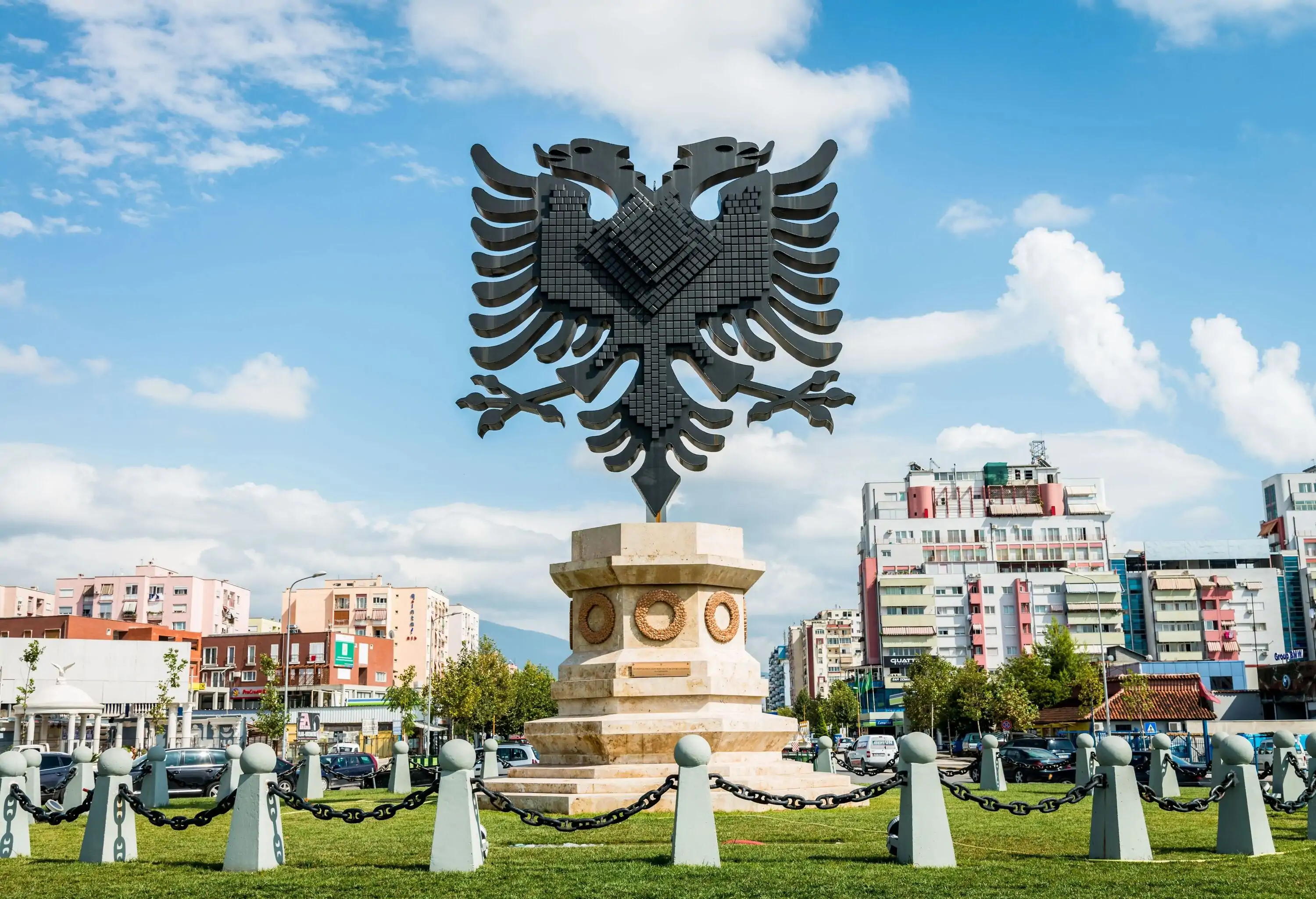 A statue of Albania's coat of arms ringed by a galvanised steel chain fence.