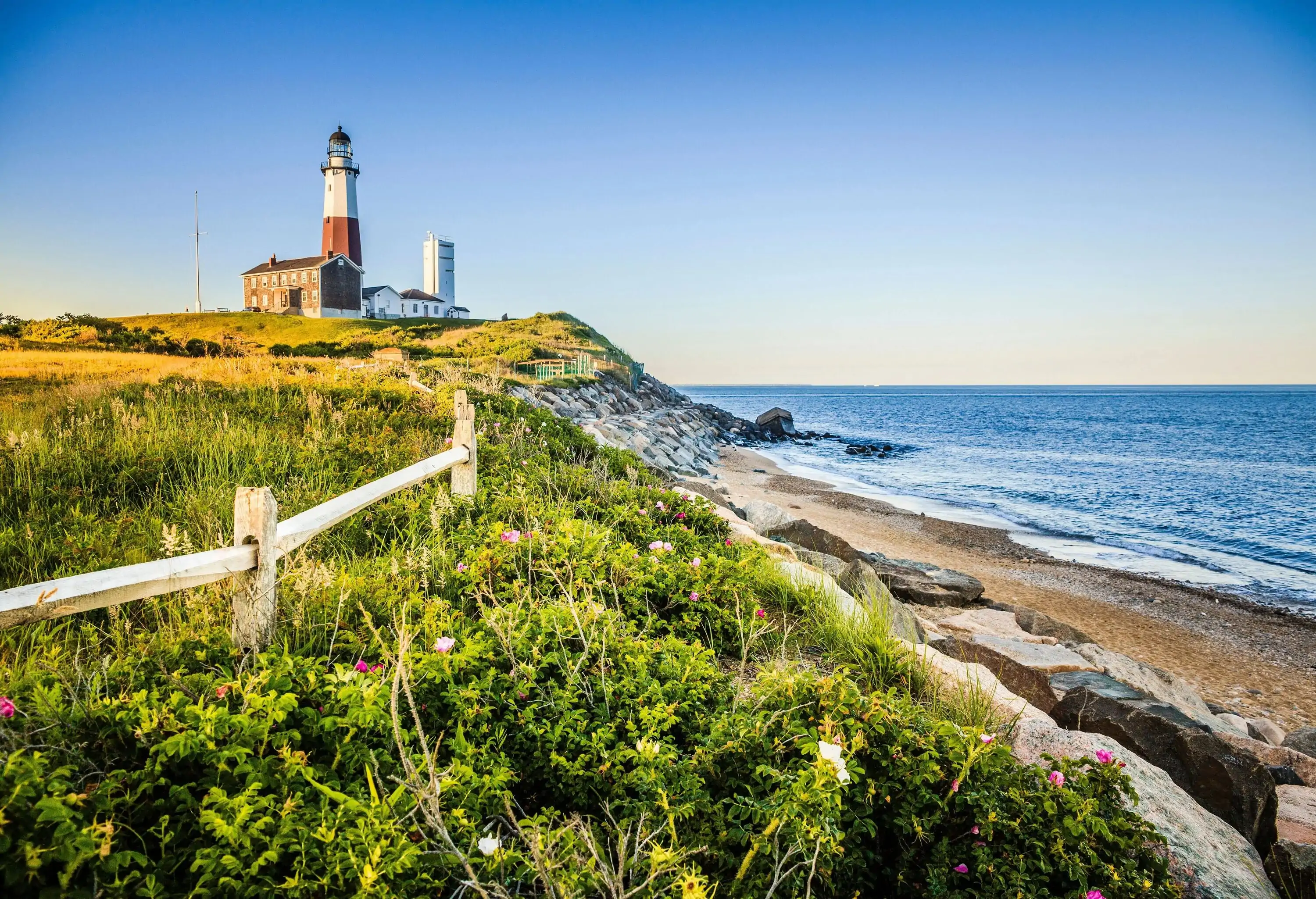 A lighthouse on a lush island surrounded by the tranquil sea under the clear blue sky.