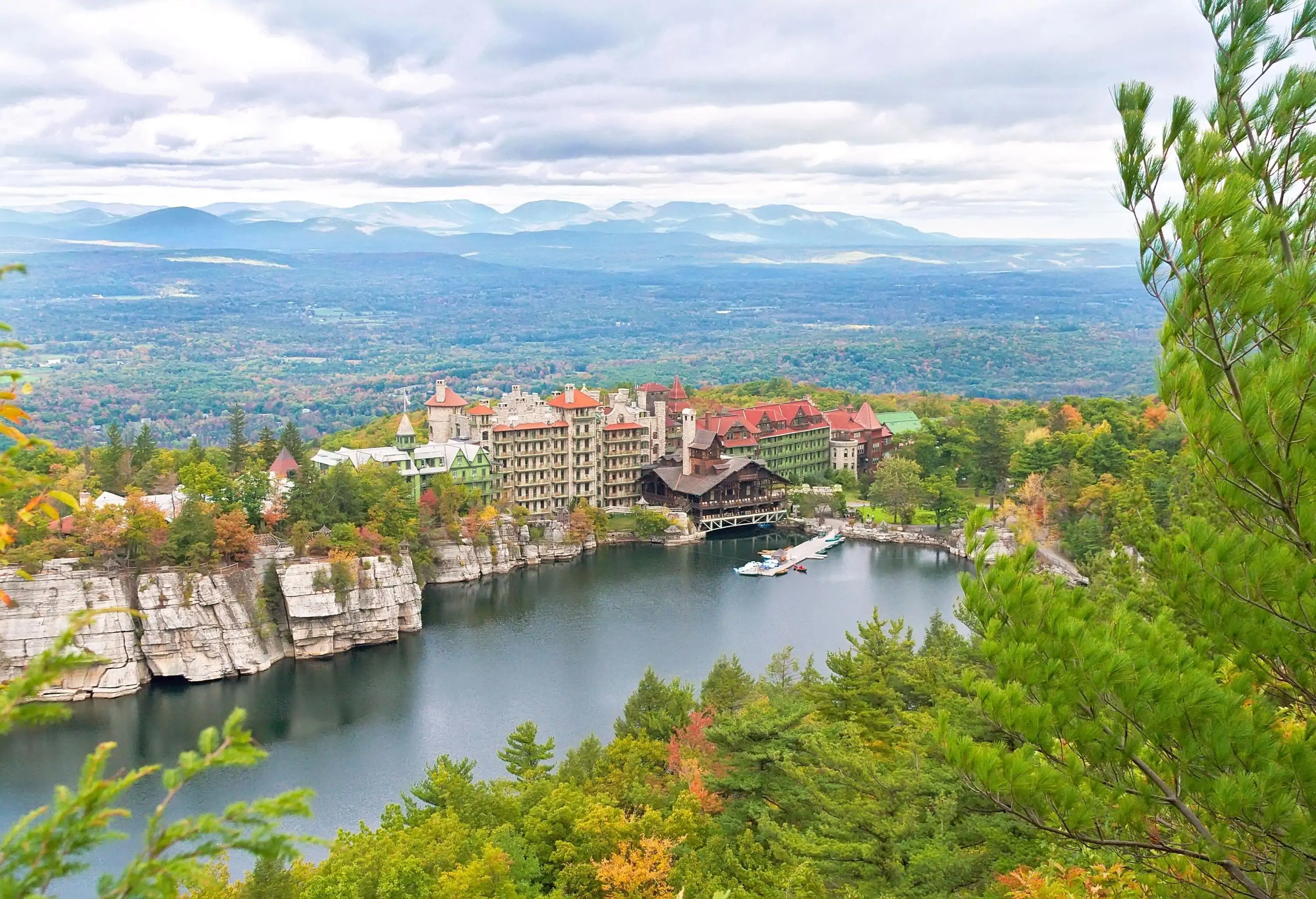 A splendid mansion house nestled on top of a mountain adjacent to a tranquil lake surrounded by tall autumn trees.