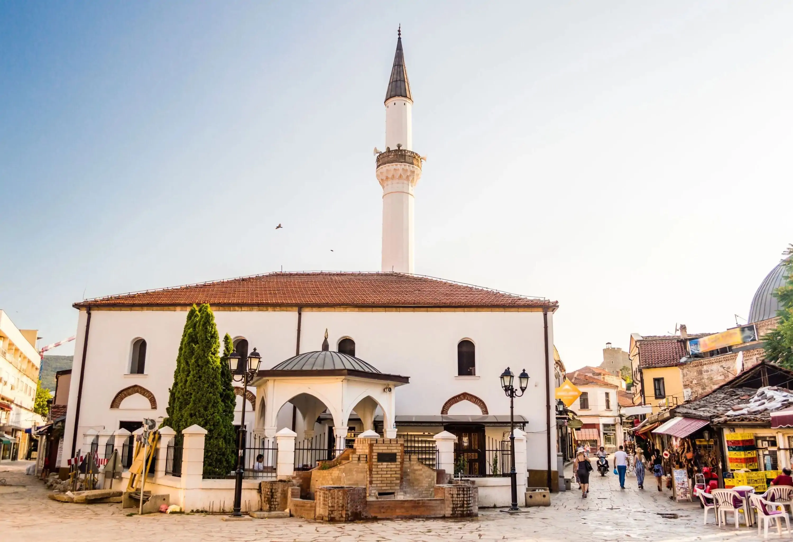 A white Ottoman Baroque mosque with an imposing minaret between the cobbled streets in an old bazaar.