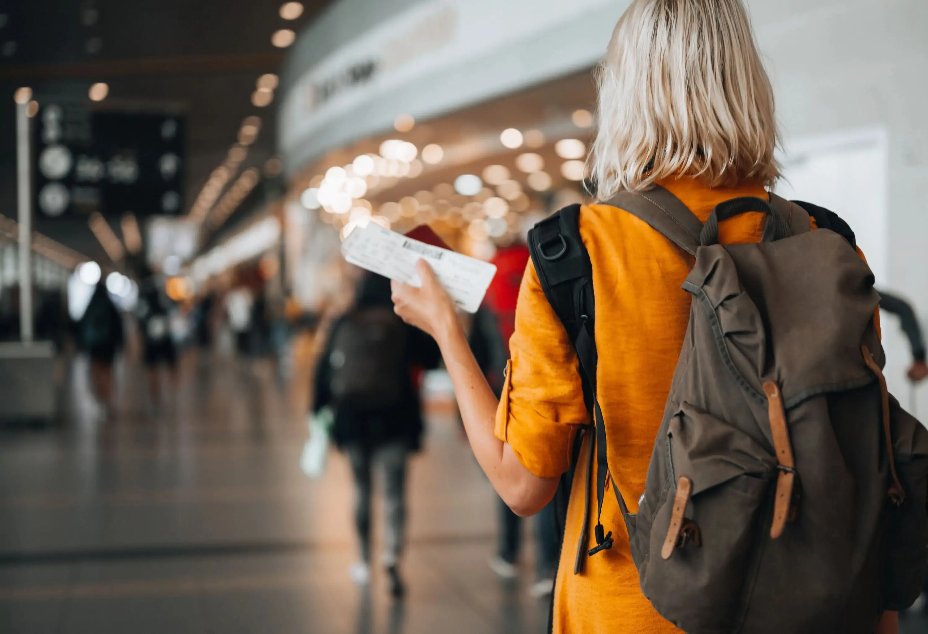 Rear view of a woman at the airport holding a passport with a boarding pass as she walks to her departure gate