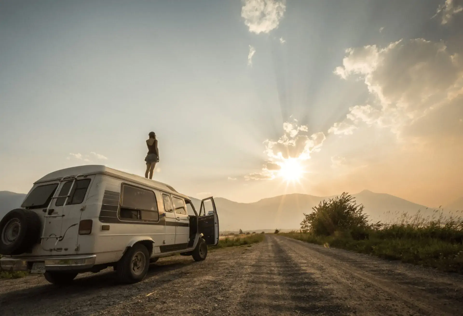 A woman stands on top of her van at sunset.