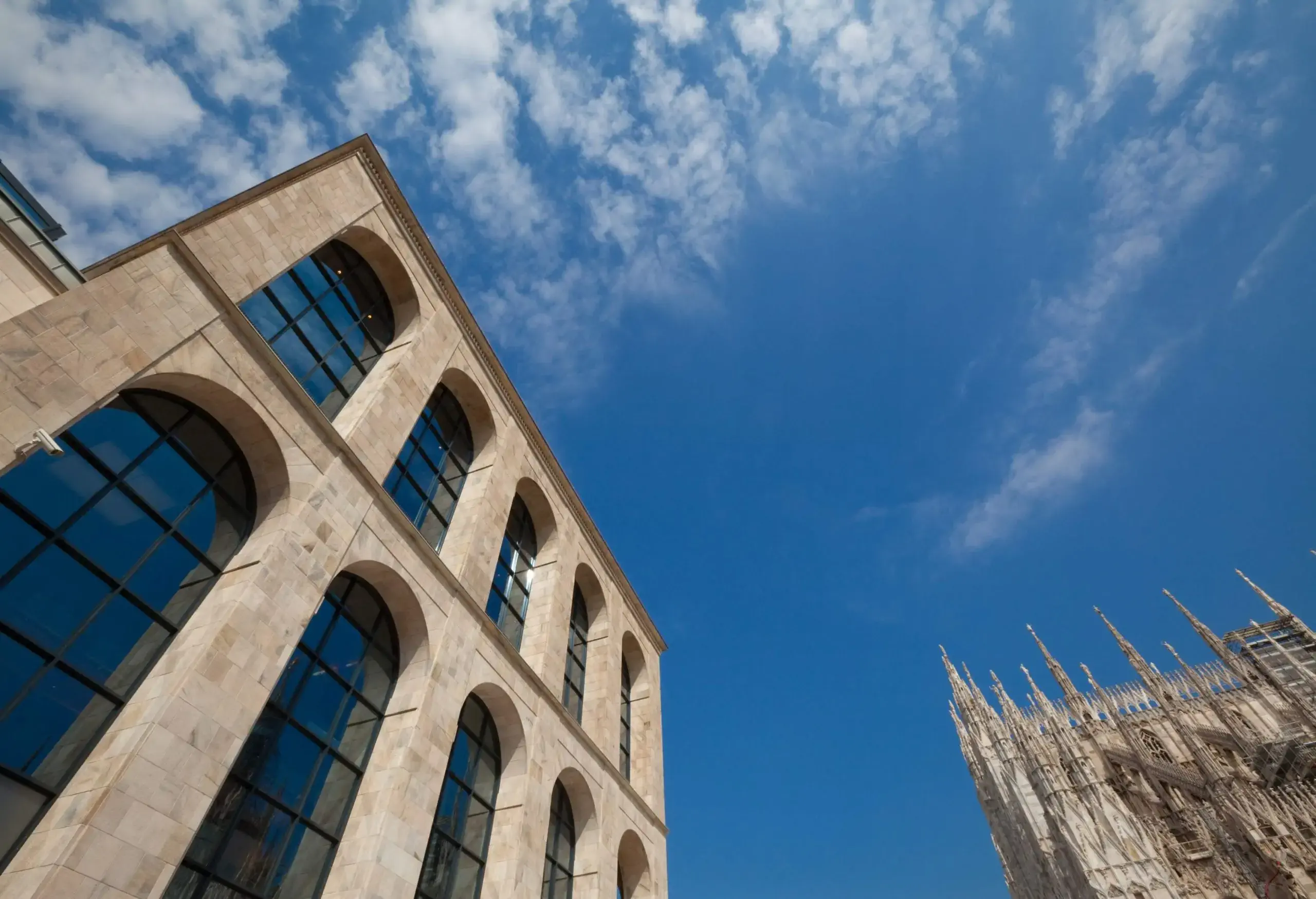 A modern building with arched glass windows and a Gothic-style structure towering into the sky.