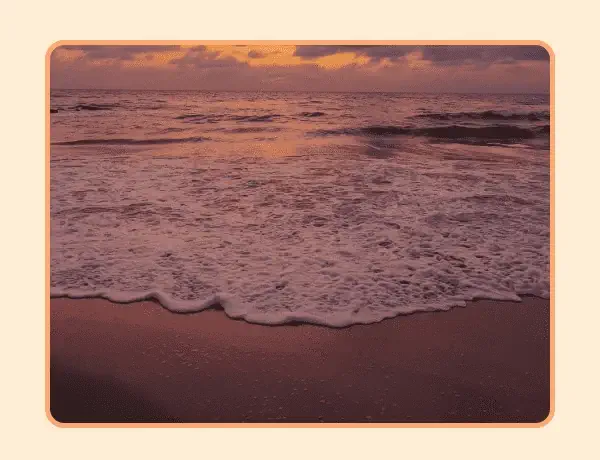 Waves gently crashing on the beach with sunset sky in the background.