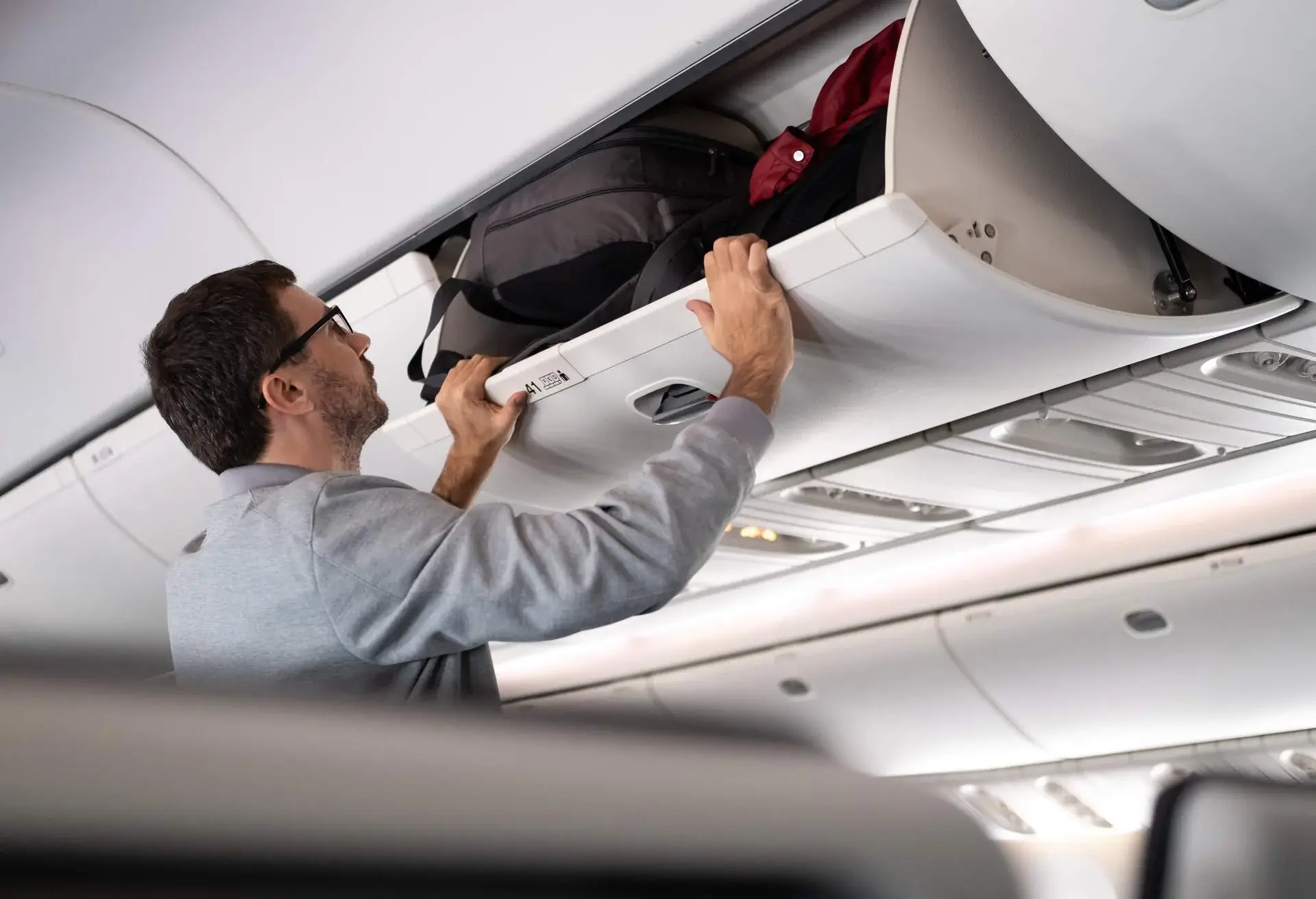 Man putting luggage into overhed locker.
