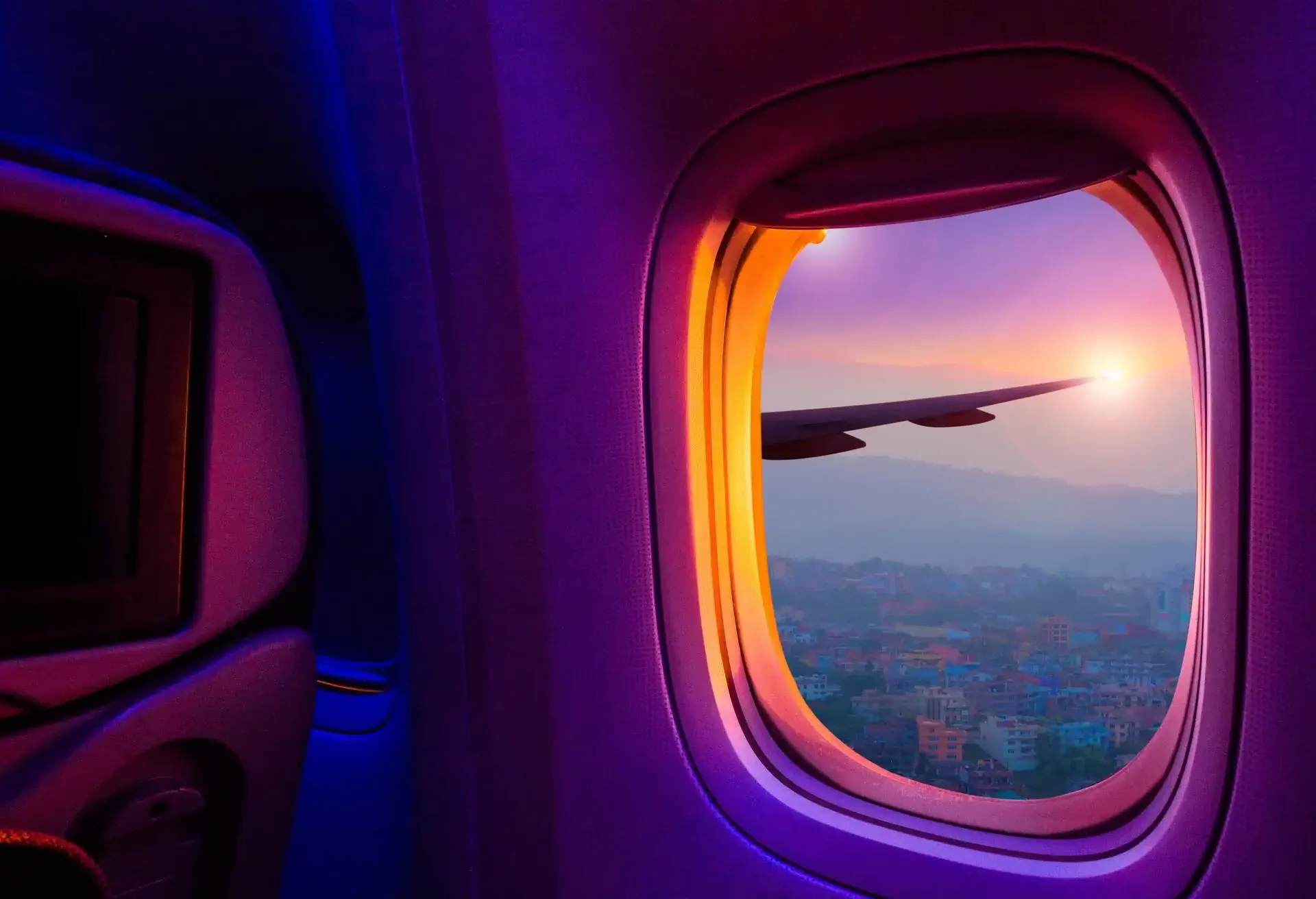 A spectacular view from a plane's window of the sun setting behind the mountain and colourful houses layered on the hill.