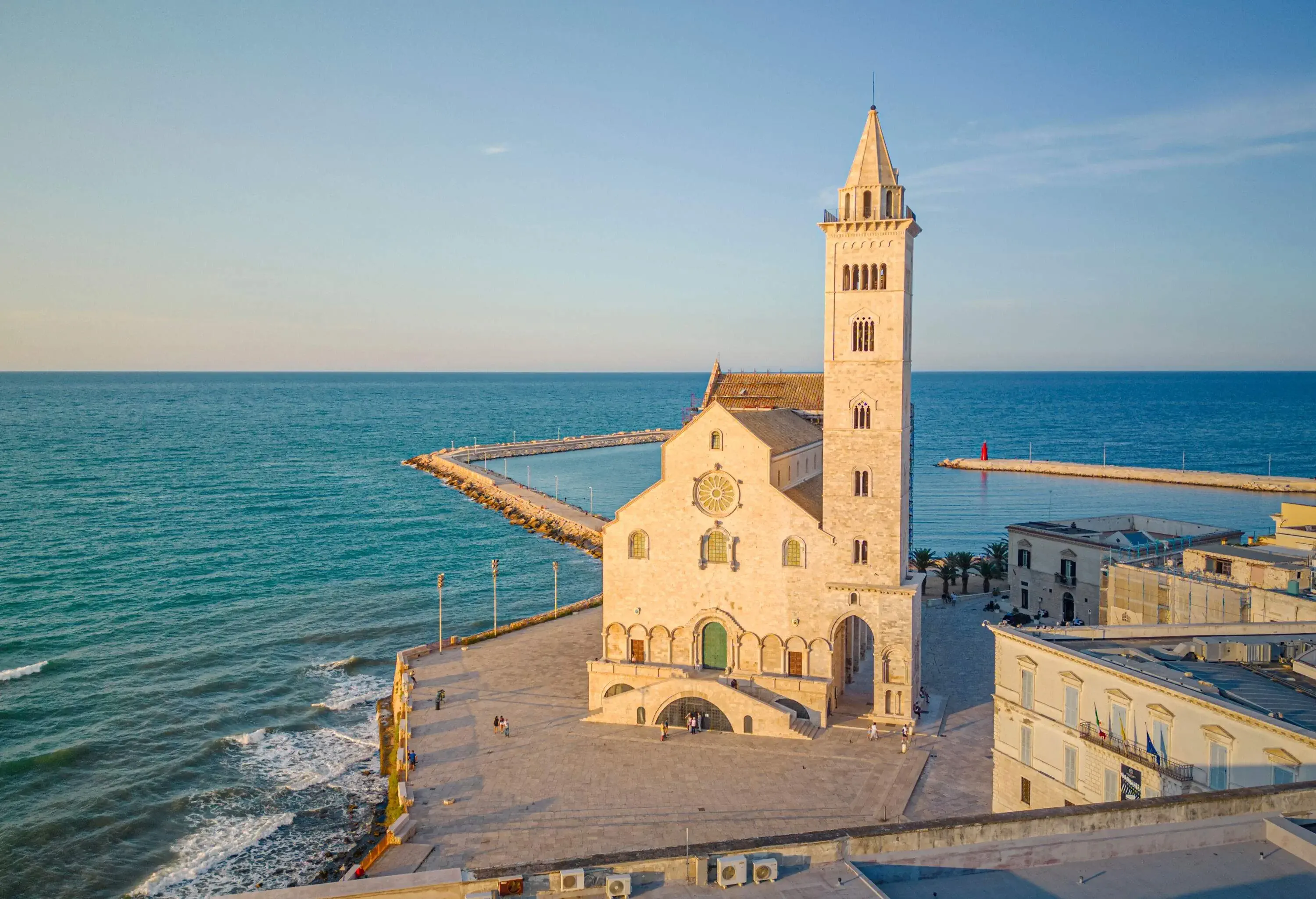 A Romanesque church with a bell tower in a cobbled square along the coast.