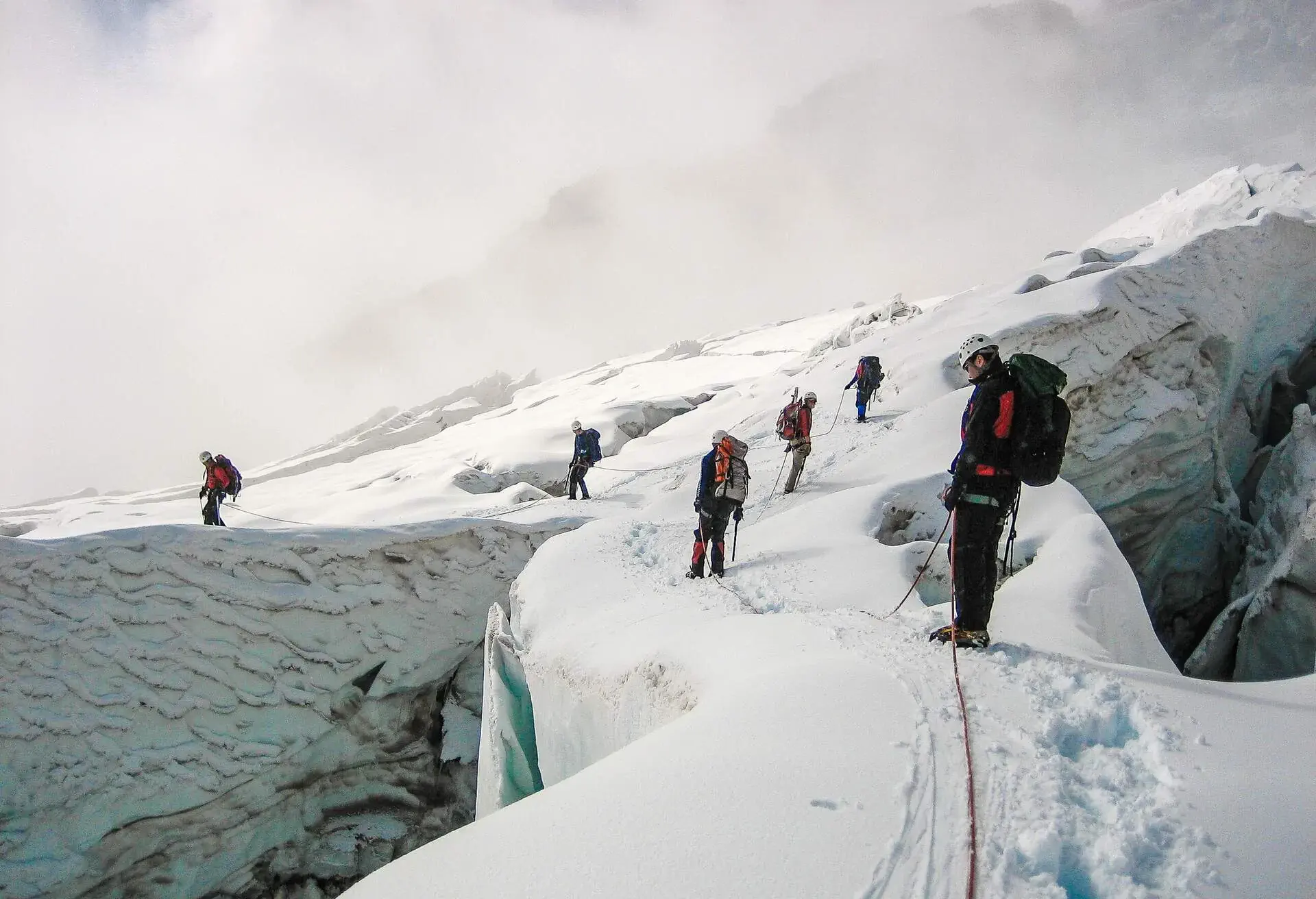 Hikers are on the snow-covered slope of the mountain on a cloudy day.
