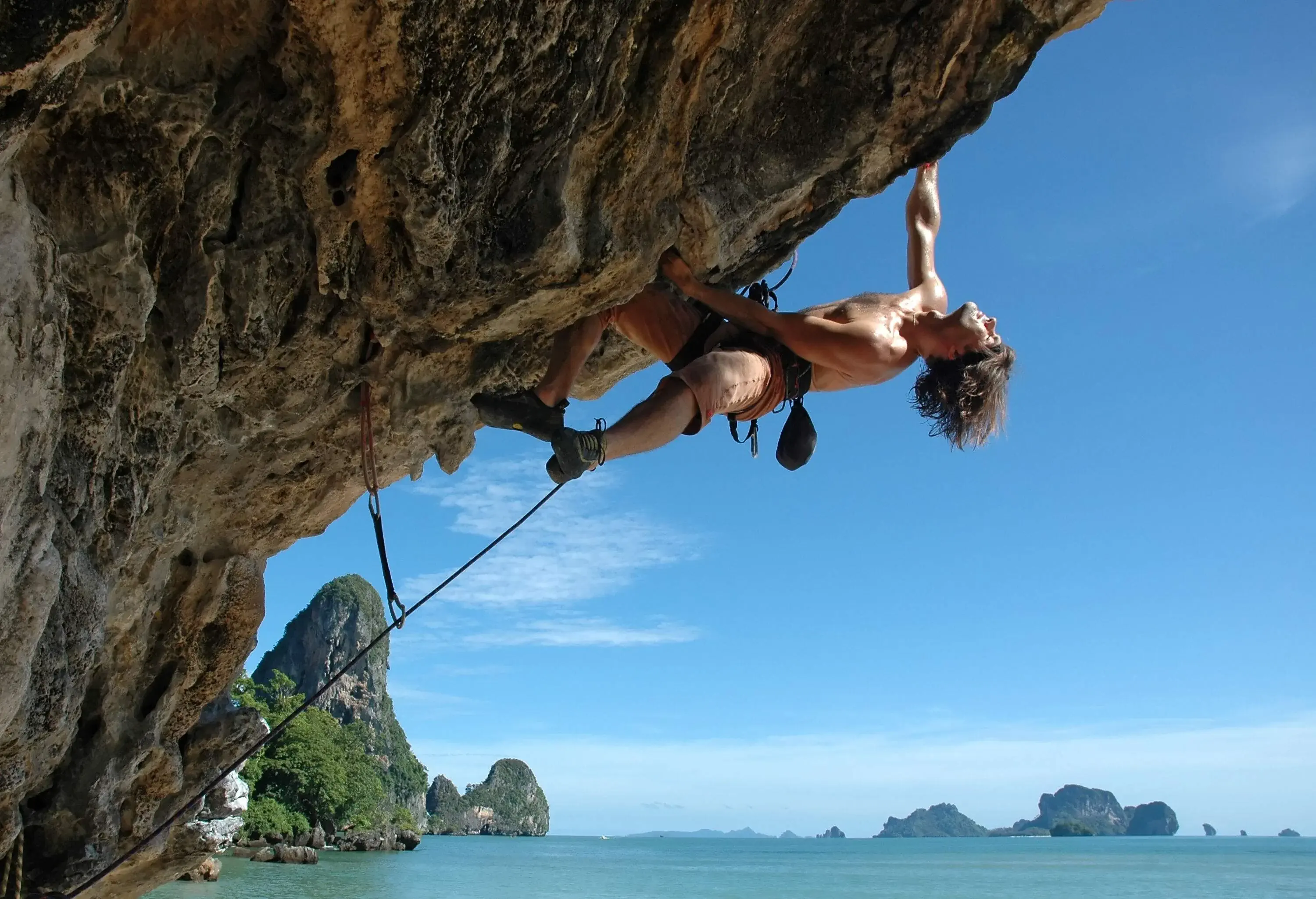 A rock climber clings on an overhanging rock wall with safety ropes.