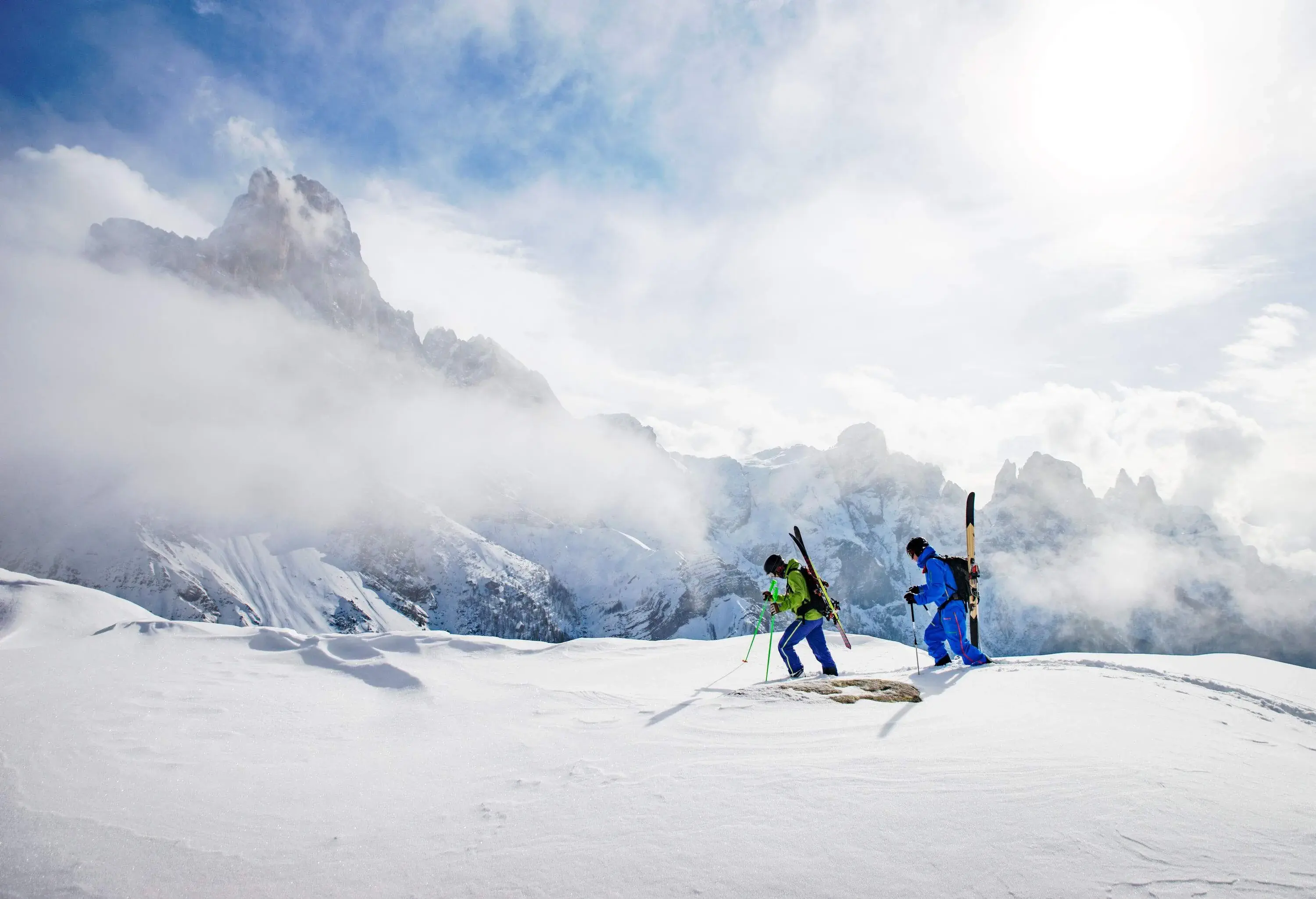 Two skiers on a snowy plateau with a view of snow-capped mountains in the fog.