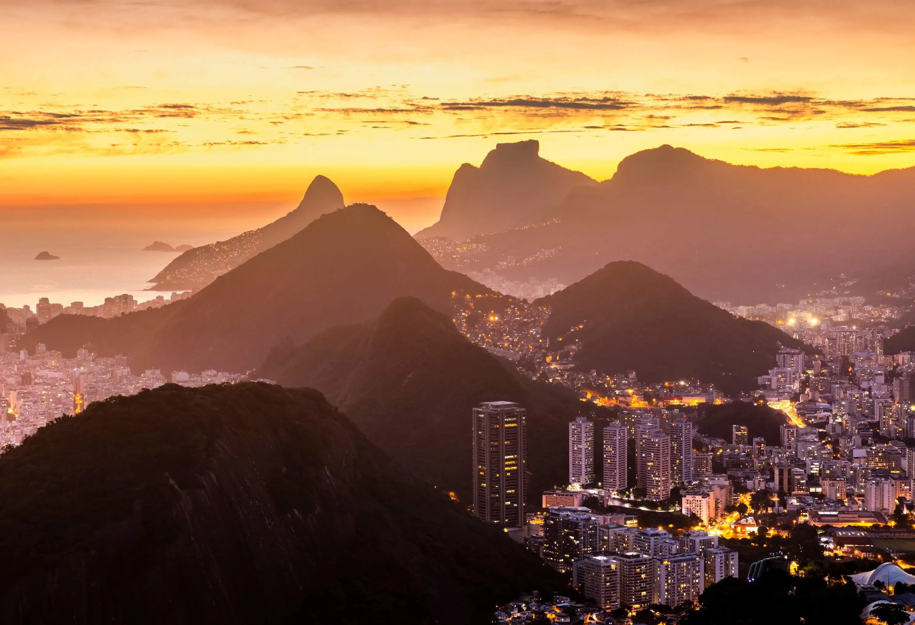 A spectacular seaside cityscape dominated by protruding hills and several rocky mountains on a dramatic sunset.