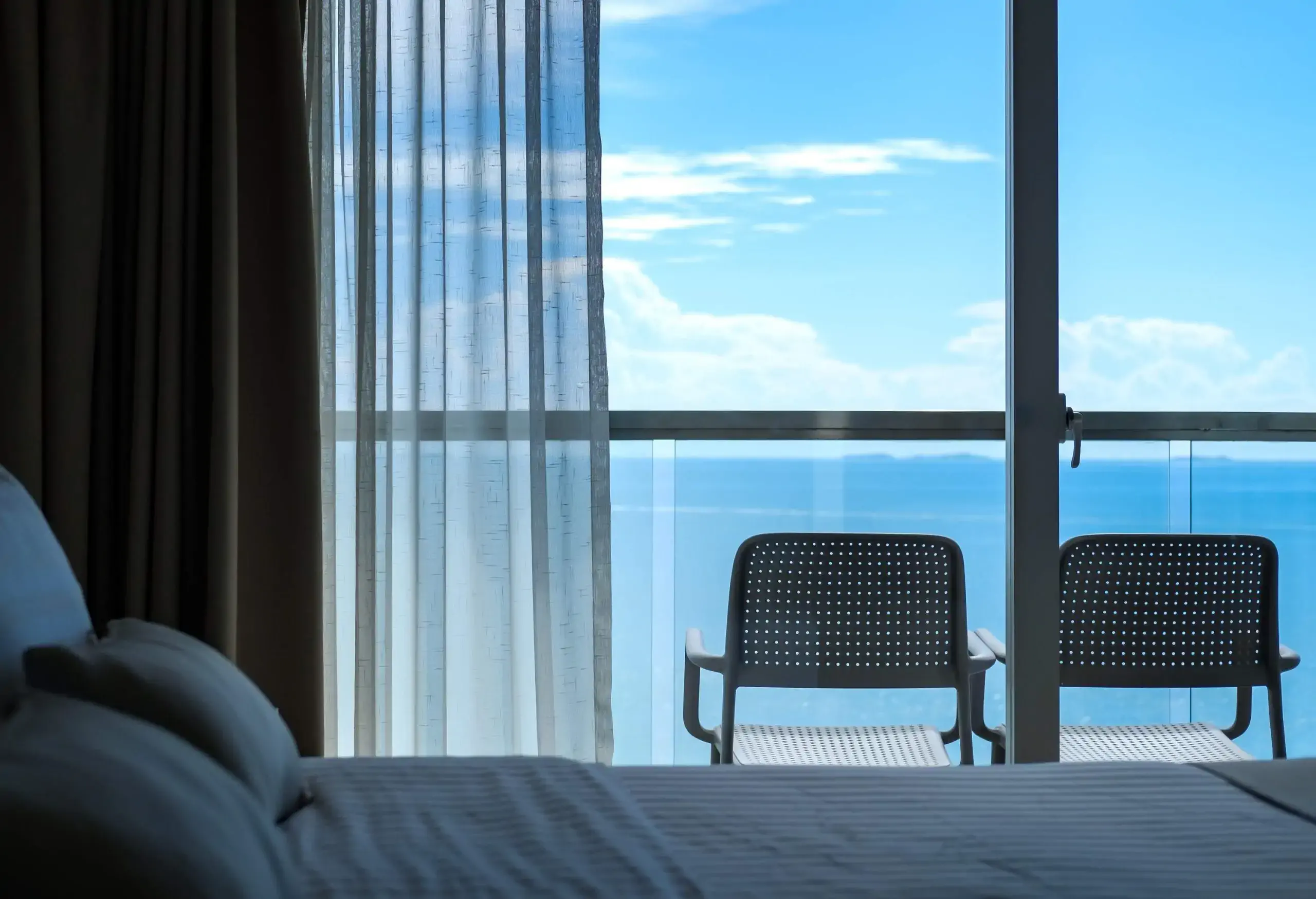 View from the bed through the window saw two chairs on the balcony, the background is sea and sky.
