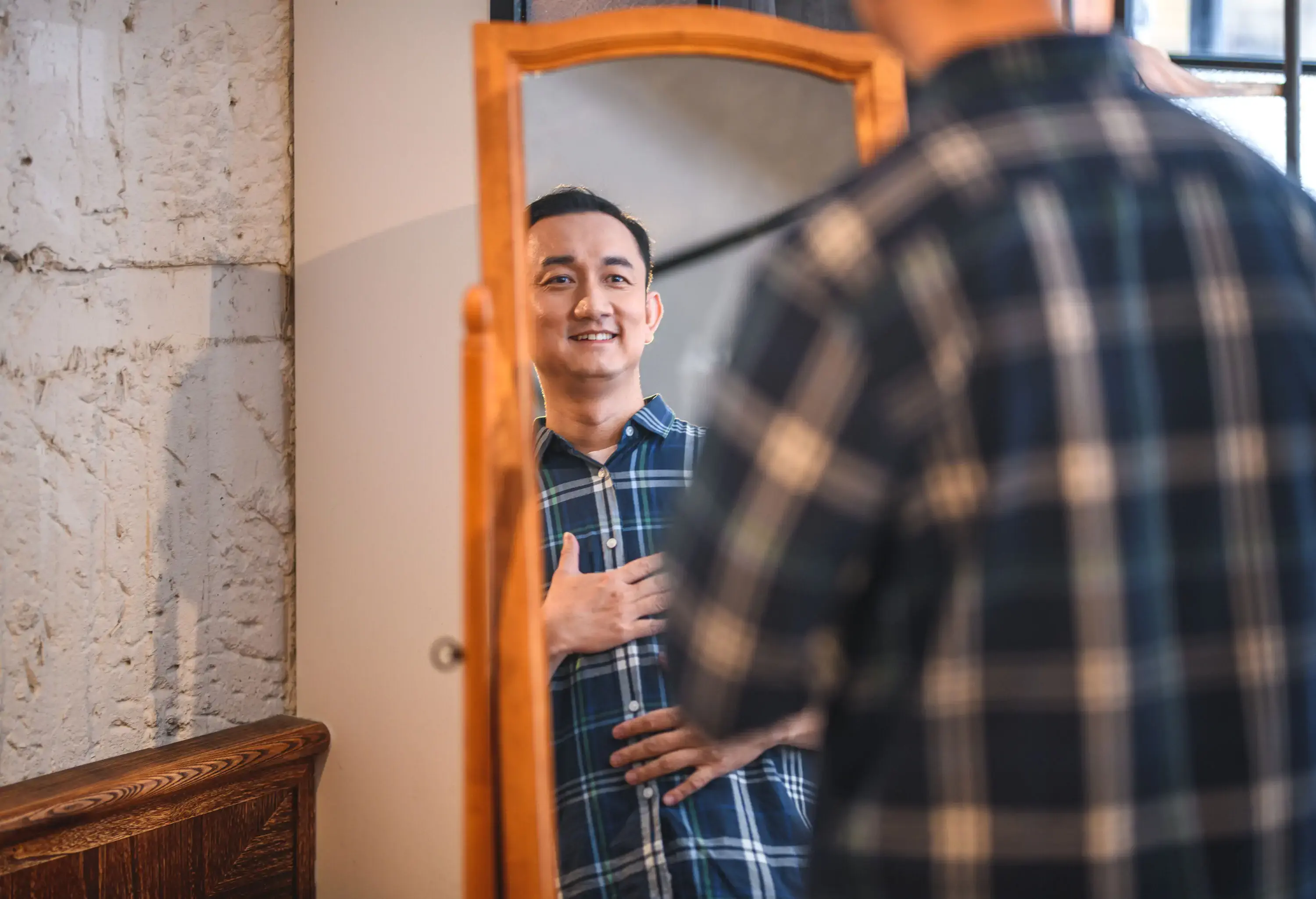 A man fitting a flannel shirt checks himself in the mirror.