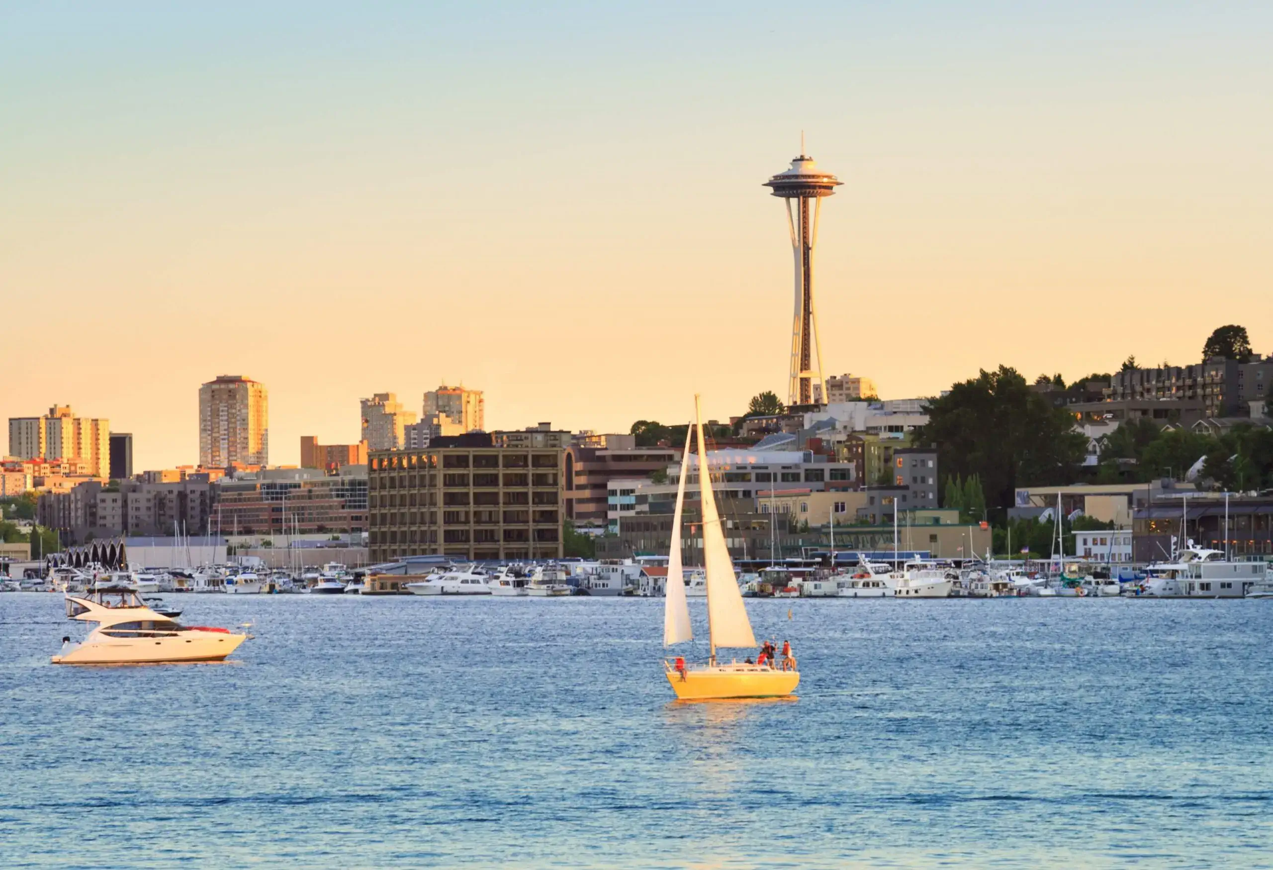 Boats gently float on the calm surface of a tranquil lake surrounded by a picturesque coastal town and a towering observation deck against the scenic twilight sky.
