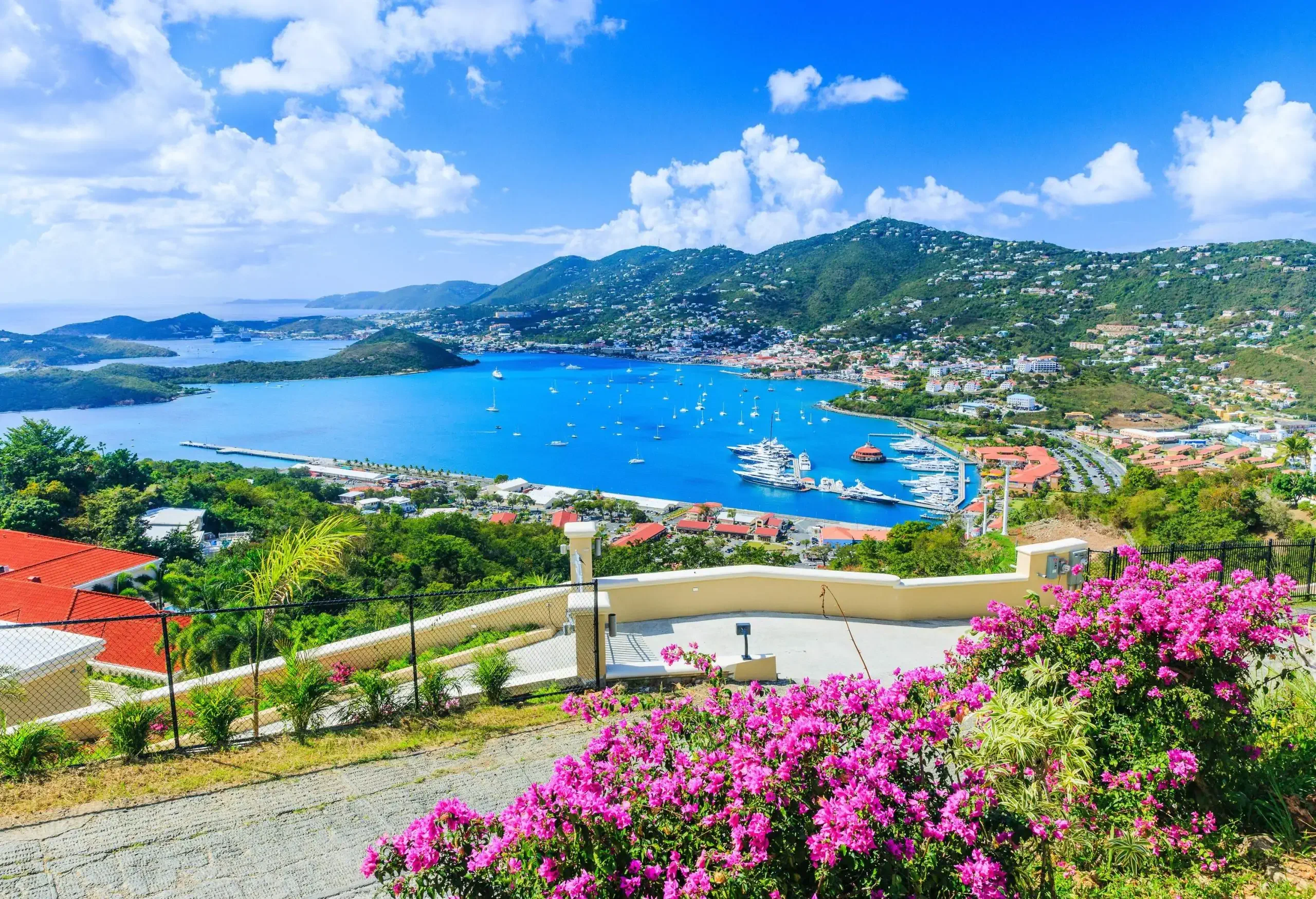 A landscape of a charming coastal town embraced by lush trees, majestic mountains, and distant islands that paint a breathtaking backdrop.