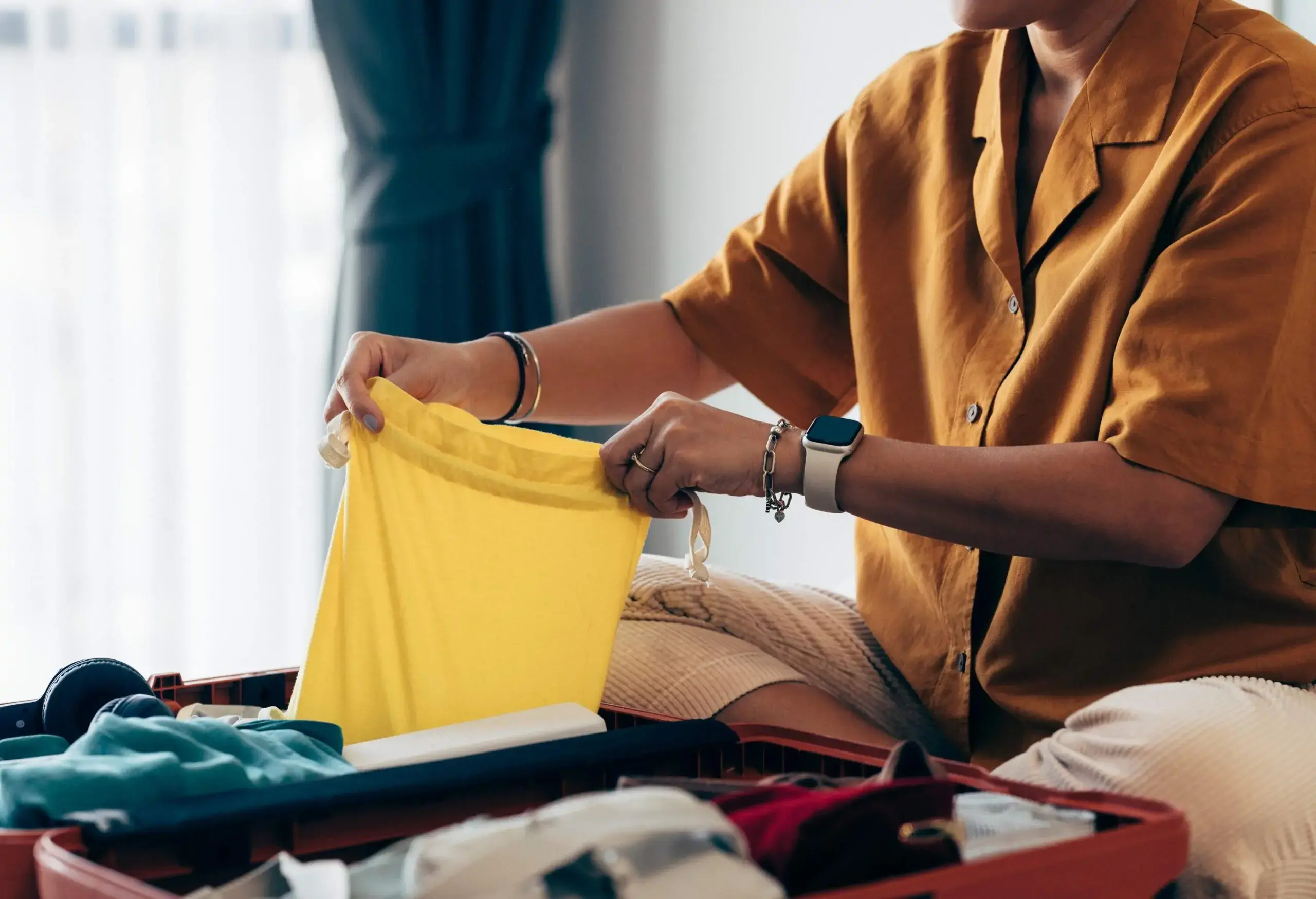 Anonymous woman sitting on the bed in a hotel room, packing her clothes in a suitcase.
