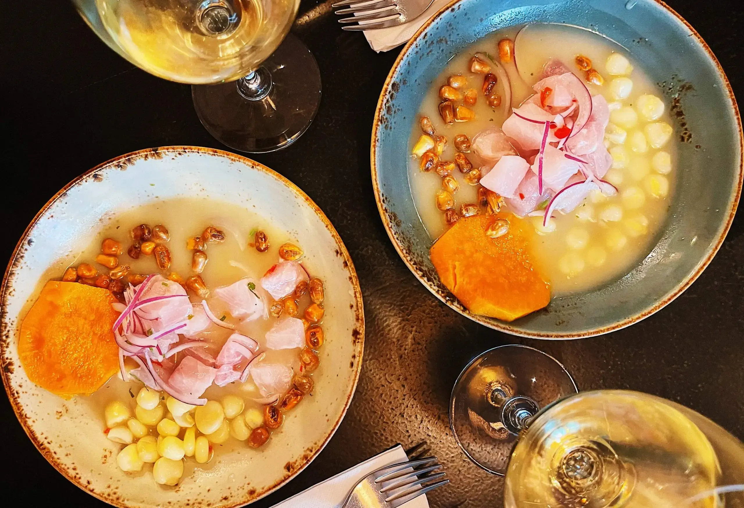 Two bowls of traditional Peruvian ceviche served with two glasses of wine.