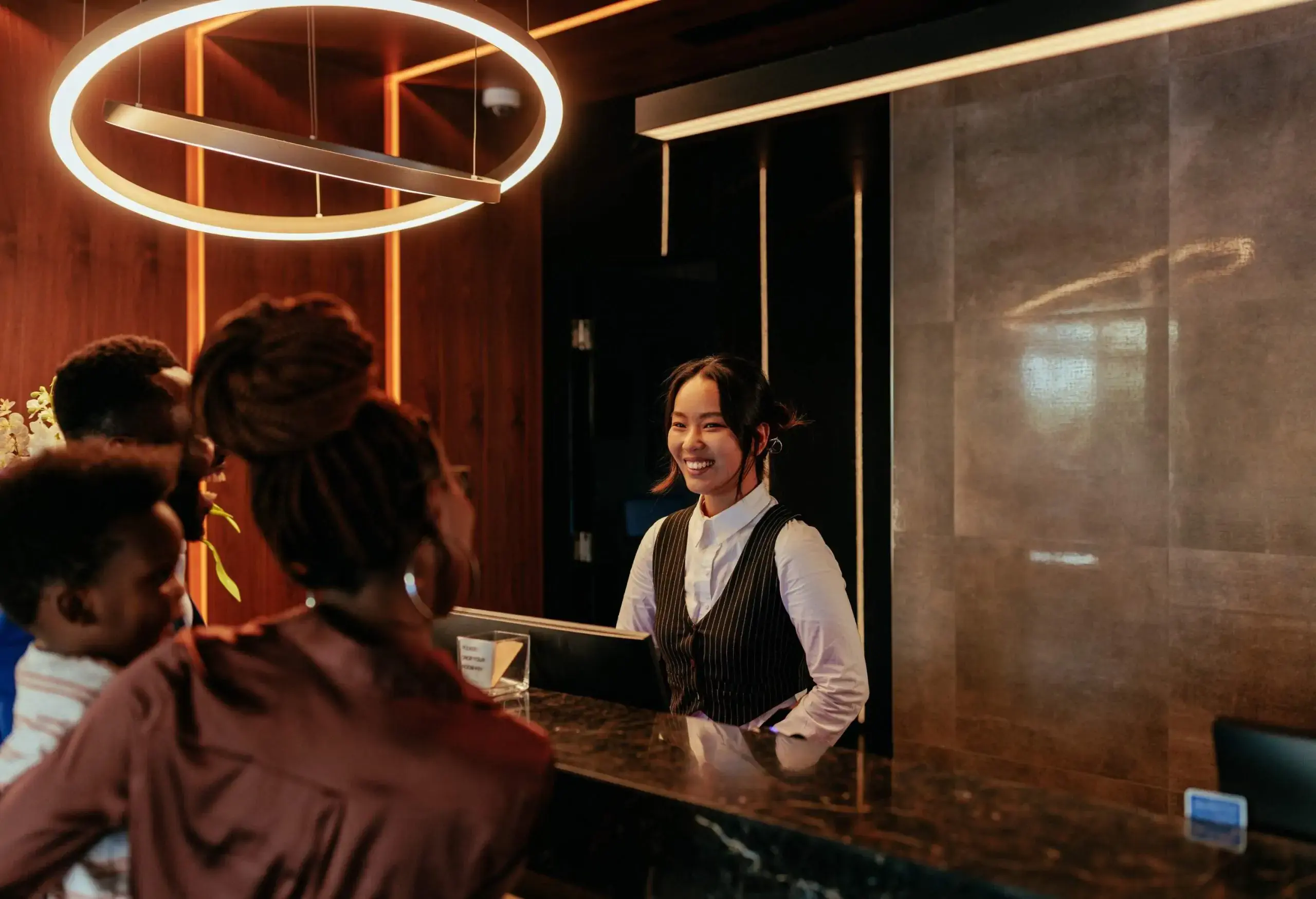 A young Asian receptionist is at the front desk of a luxurious hotel talking to her African American hotel guests.