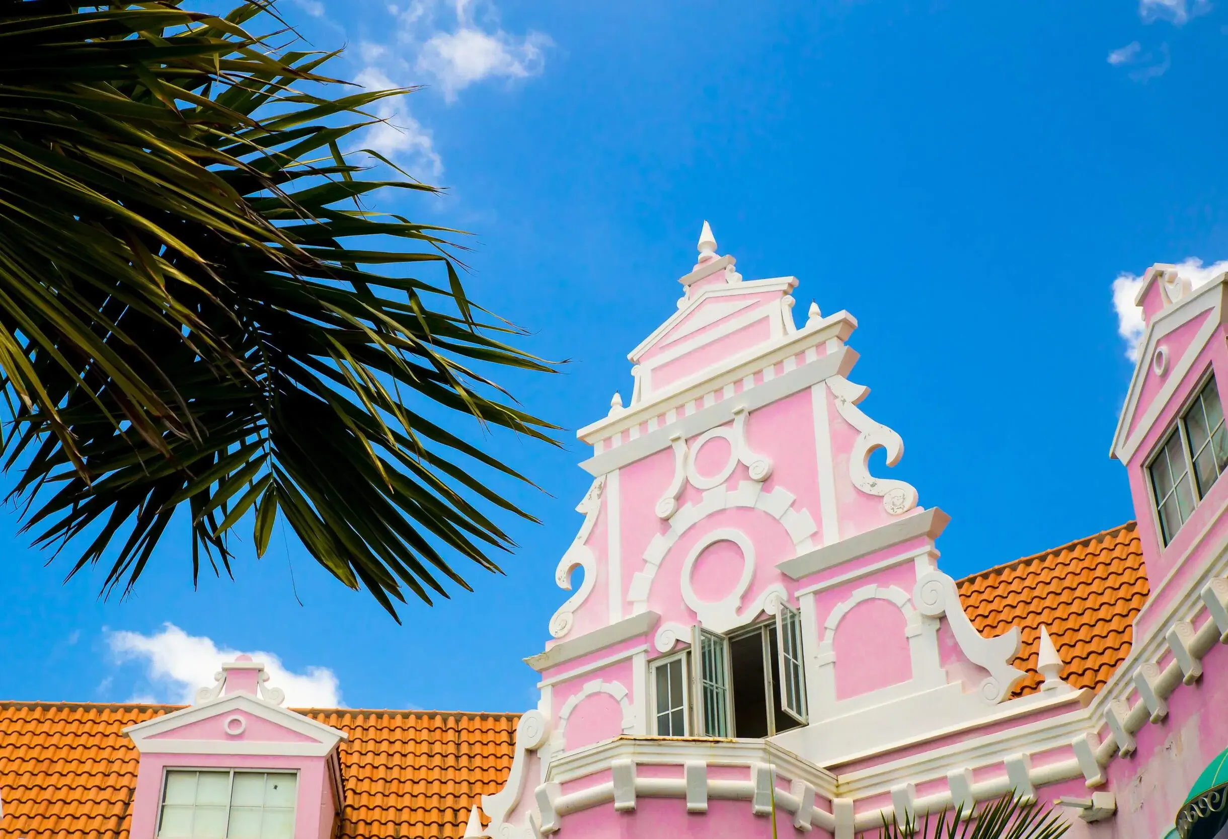 An ornate baby-pink window on an orange tile roof.
