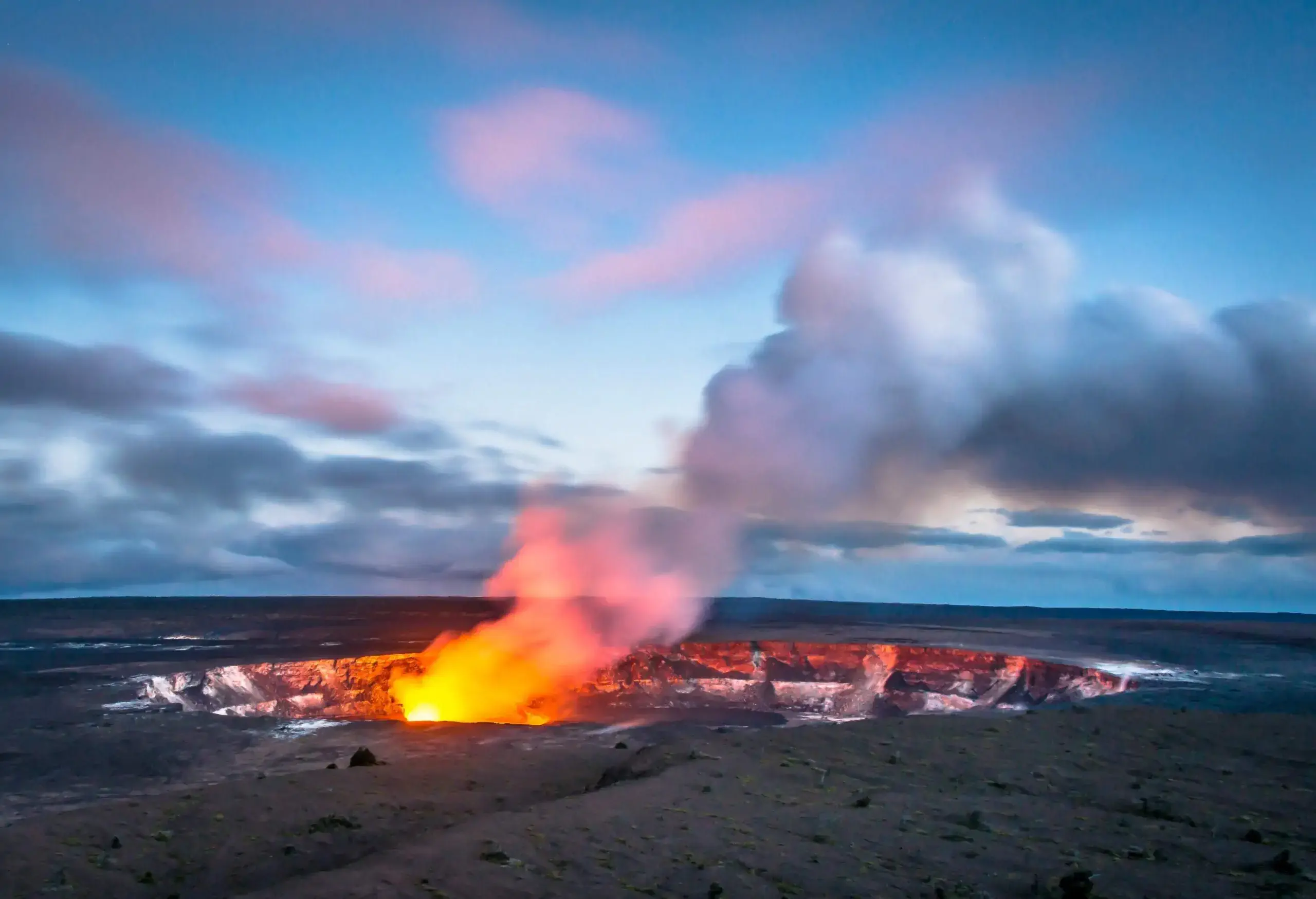 Steam plume rising from a crater against the cloudy blue sky.