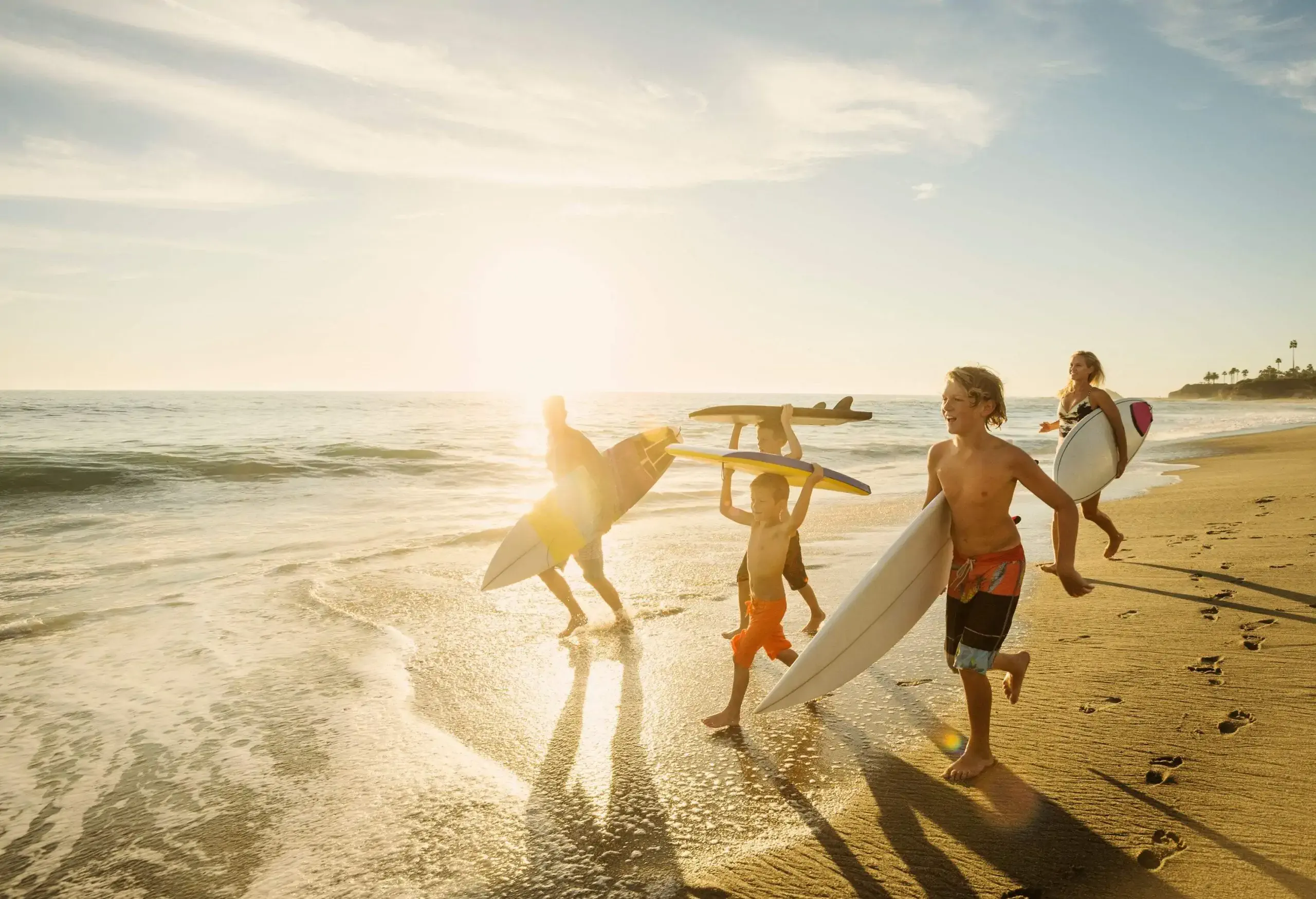 Family of surfers carrying surfboards along the beach