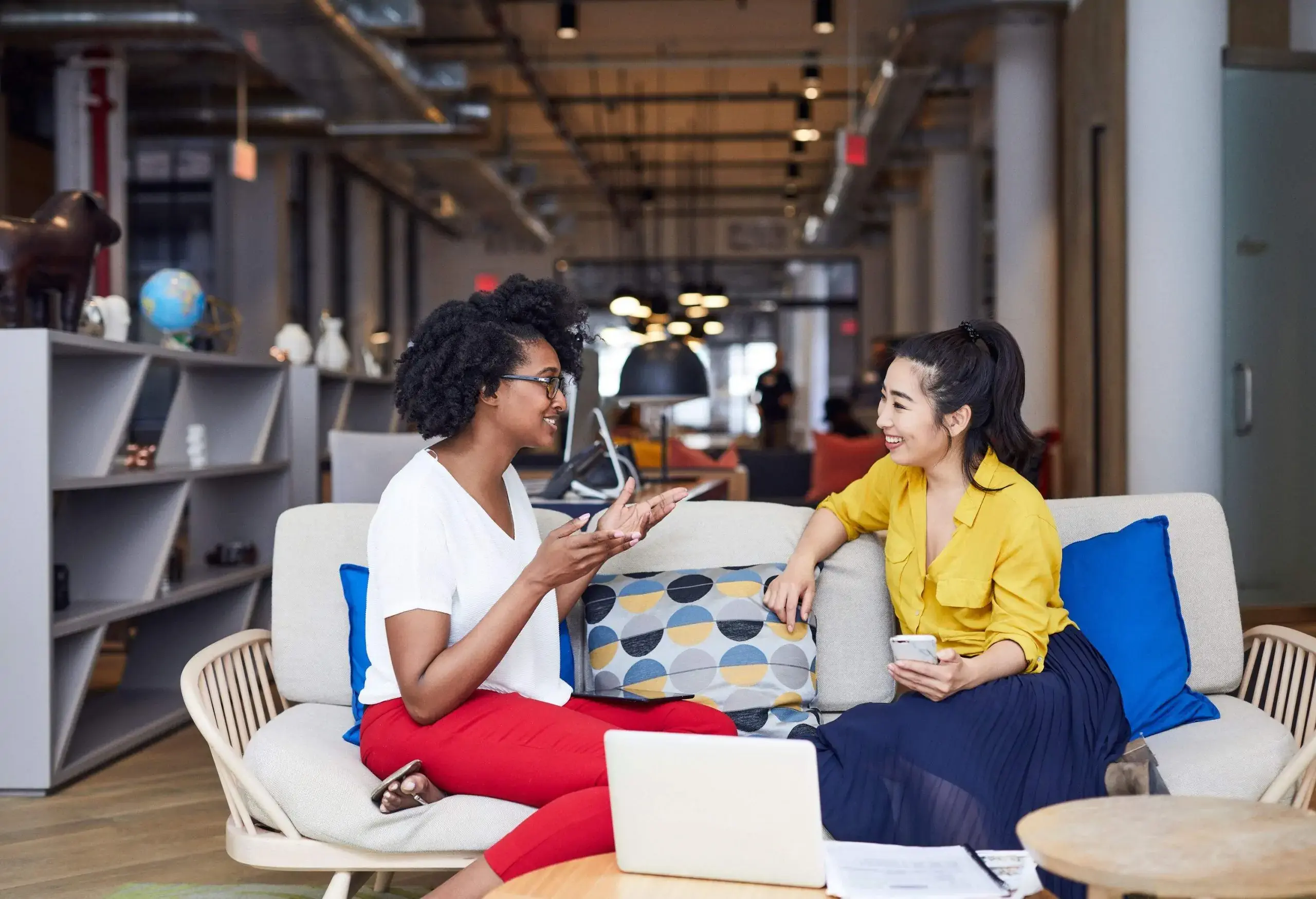 Two women chatting animatedly while sitting on a couch.