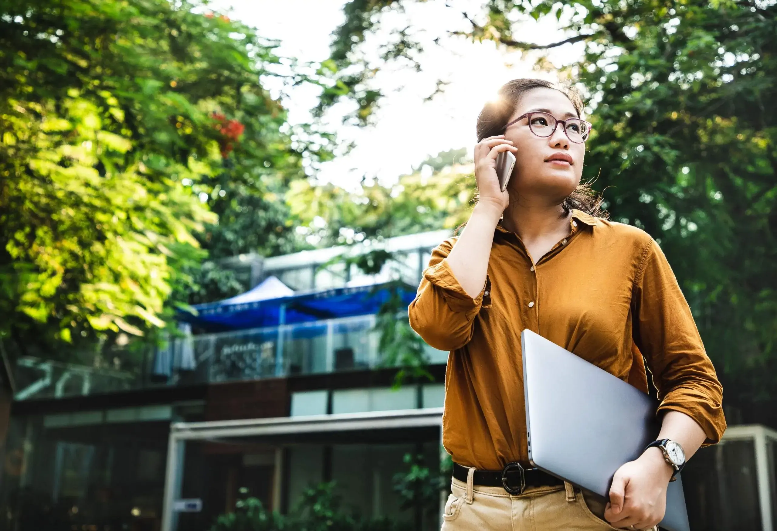 A woman wearing eyeglasses carrying a laptop and talking on the phone.