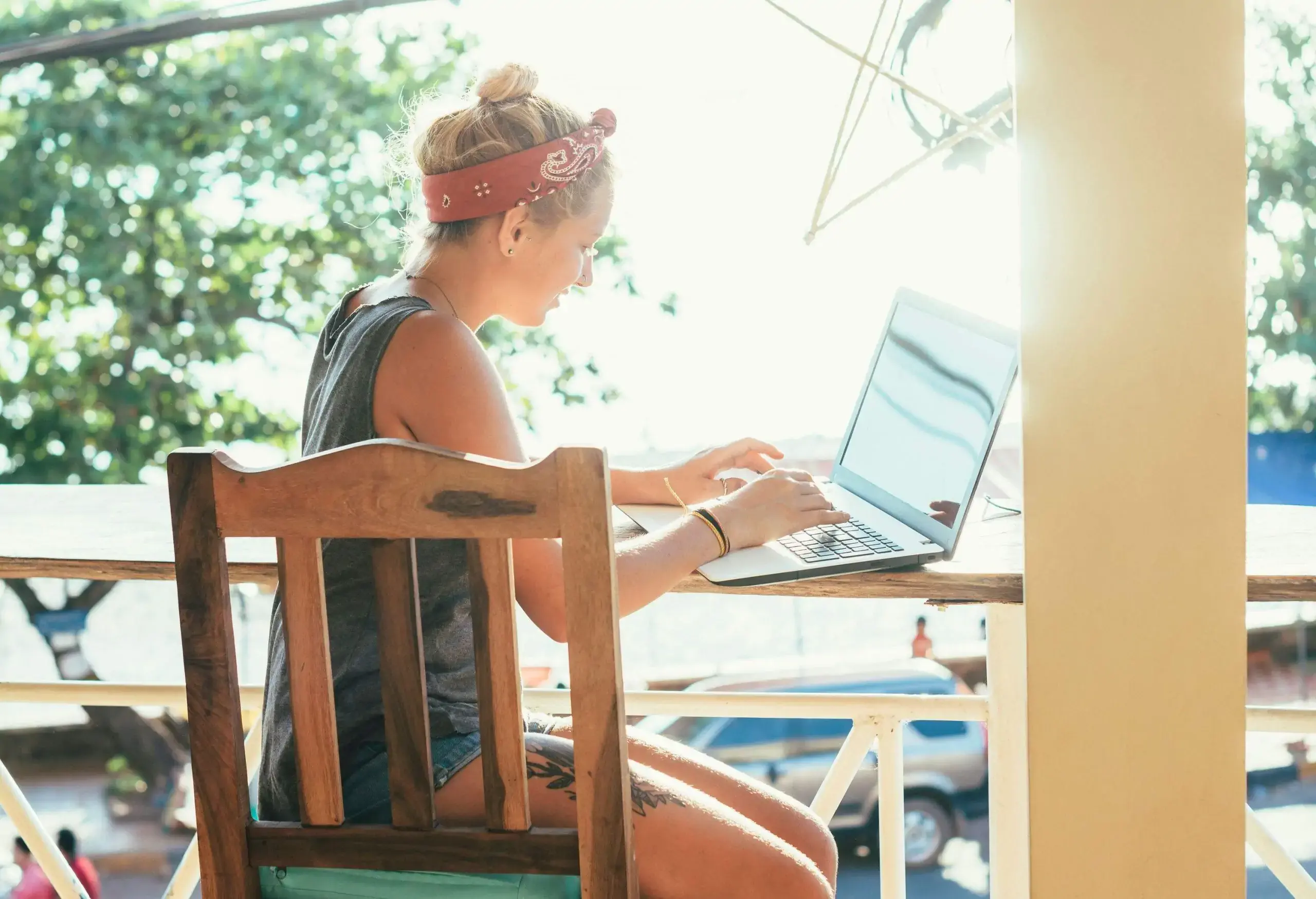 A lady backpacker works on her laptop on the sunlit balcony.