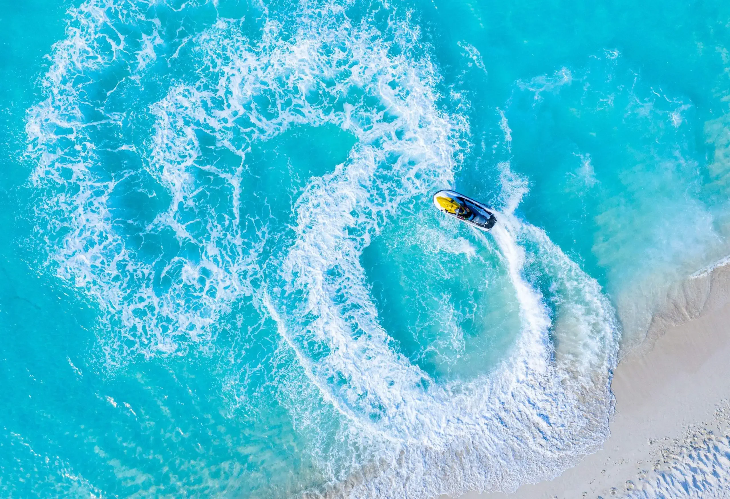 Waves are created by a jetski racing in circles on a clear beach.