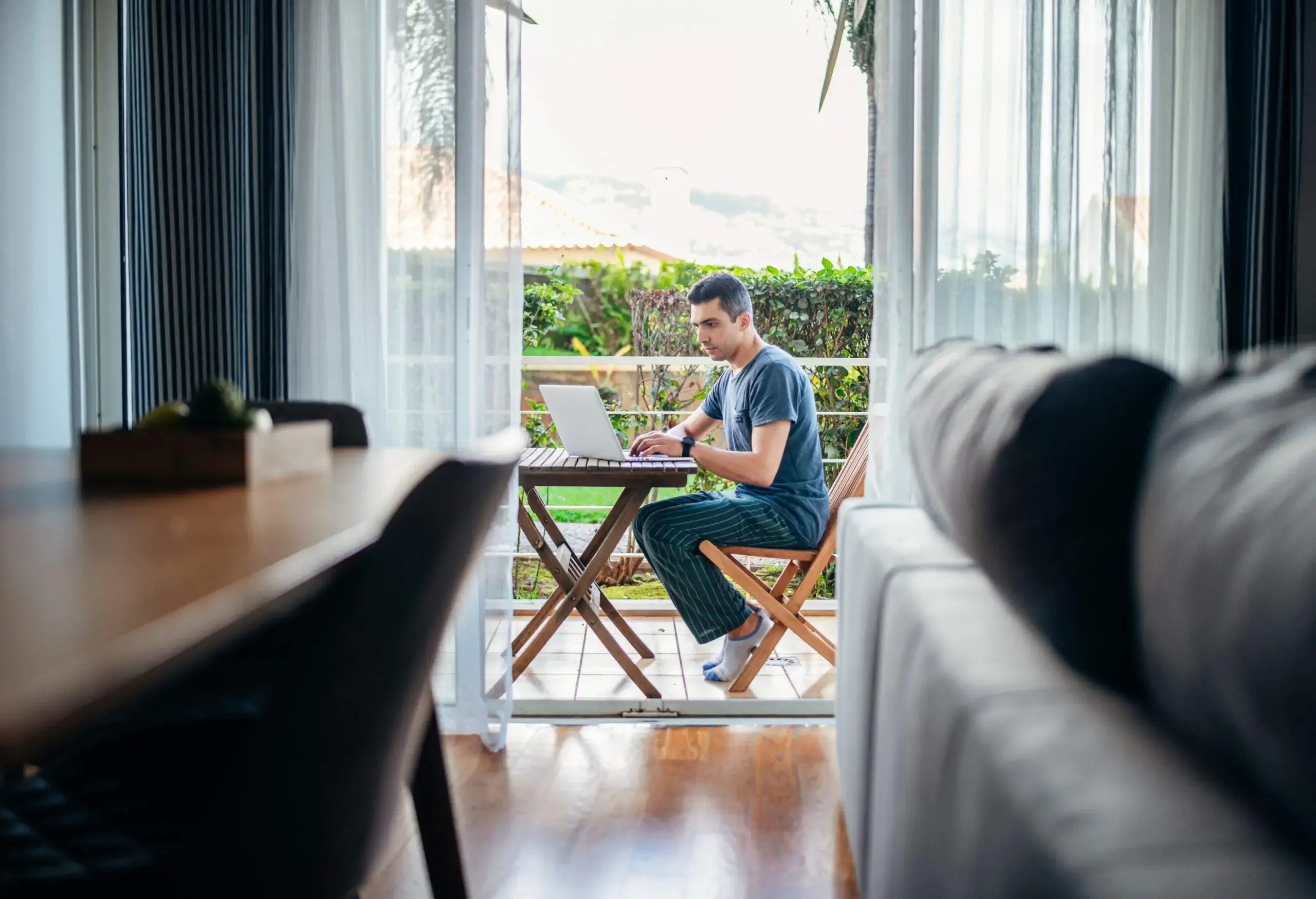 Man working from home on laptop and relaxing on balcony.