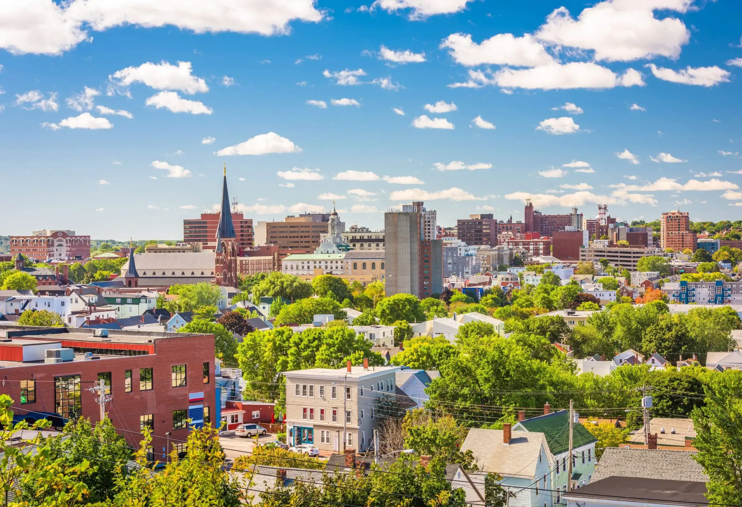 The skyline of a city is made up of tall buildings, steeples, and gable-roofed dwellings that are complemented by a beautiful sky.