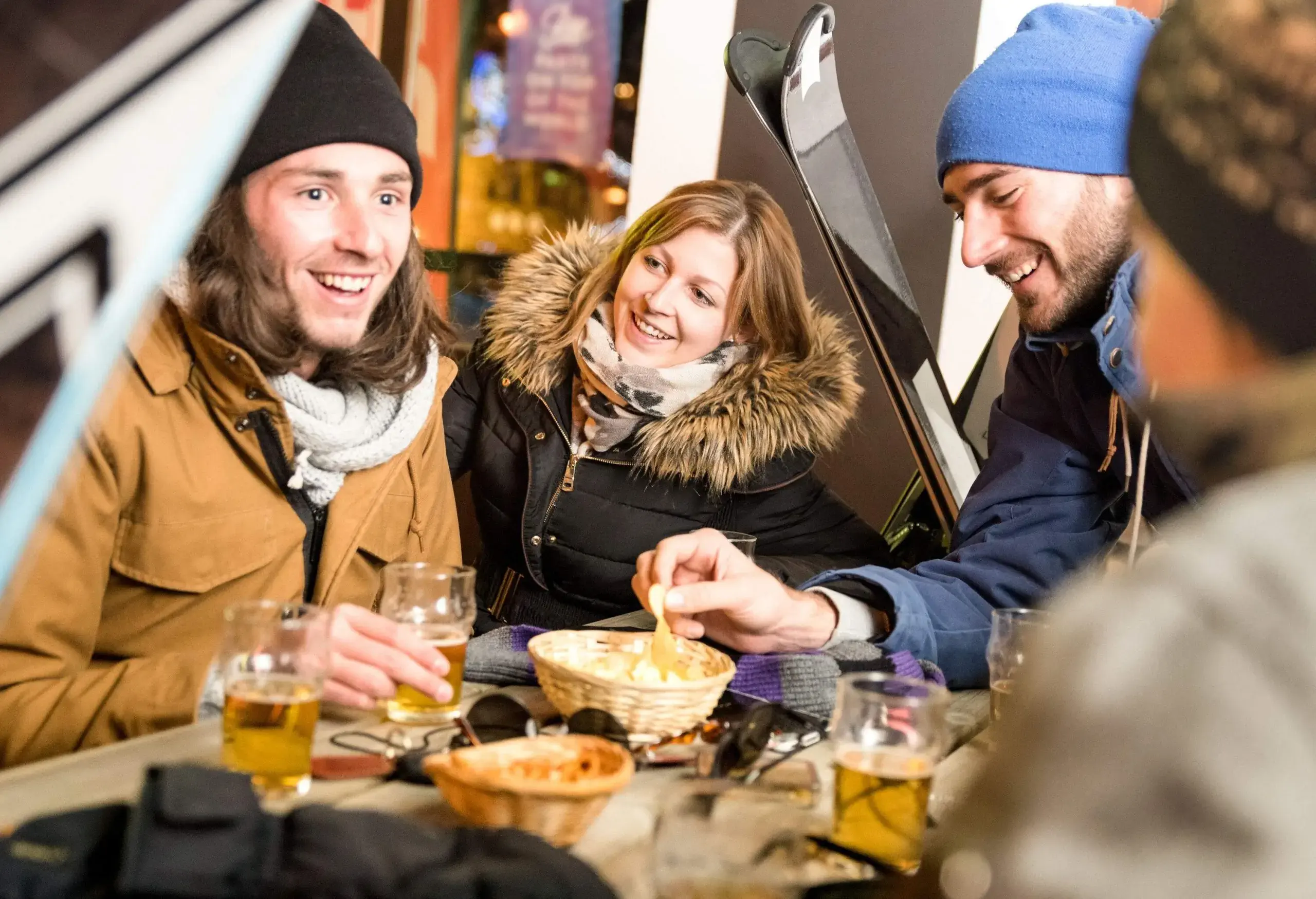 A group of friends chatting happily over glasses of beers and chips.