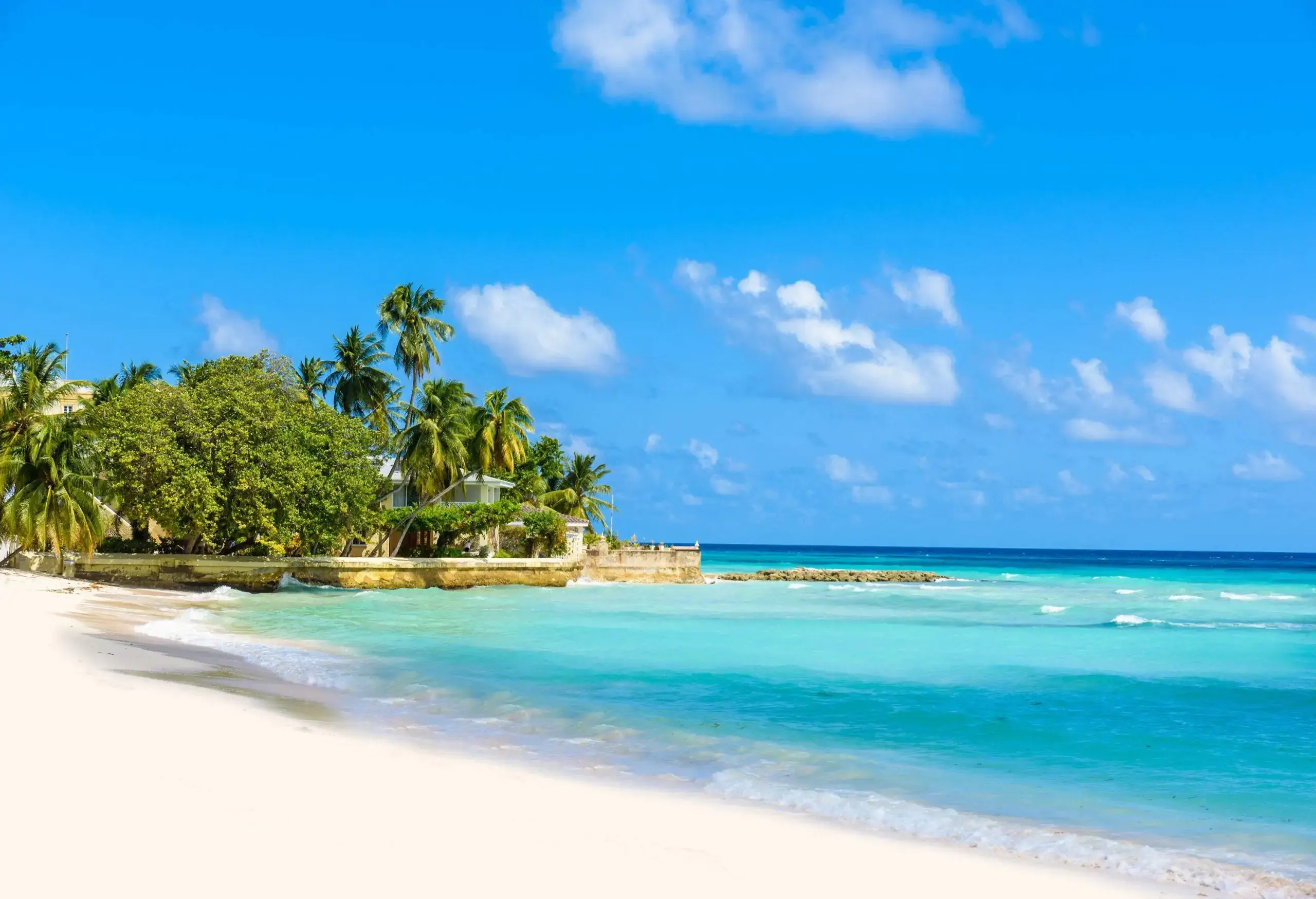 An inviting beachscape with white sand and aquamarine waters under a sunny sky.