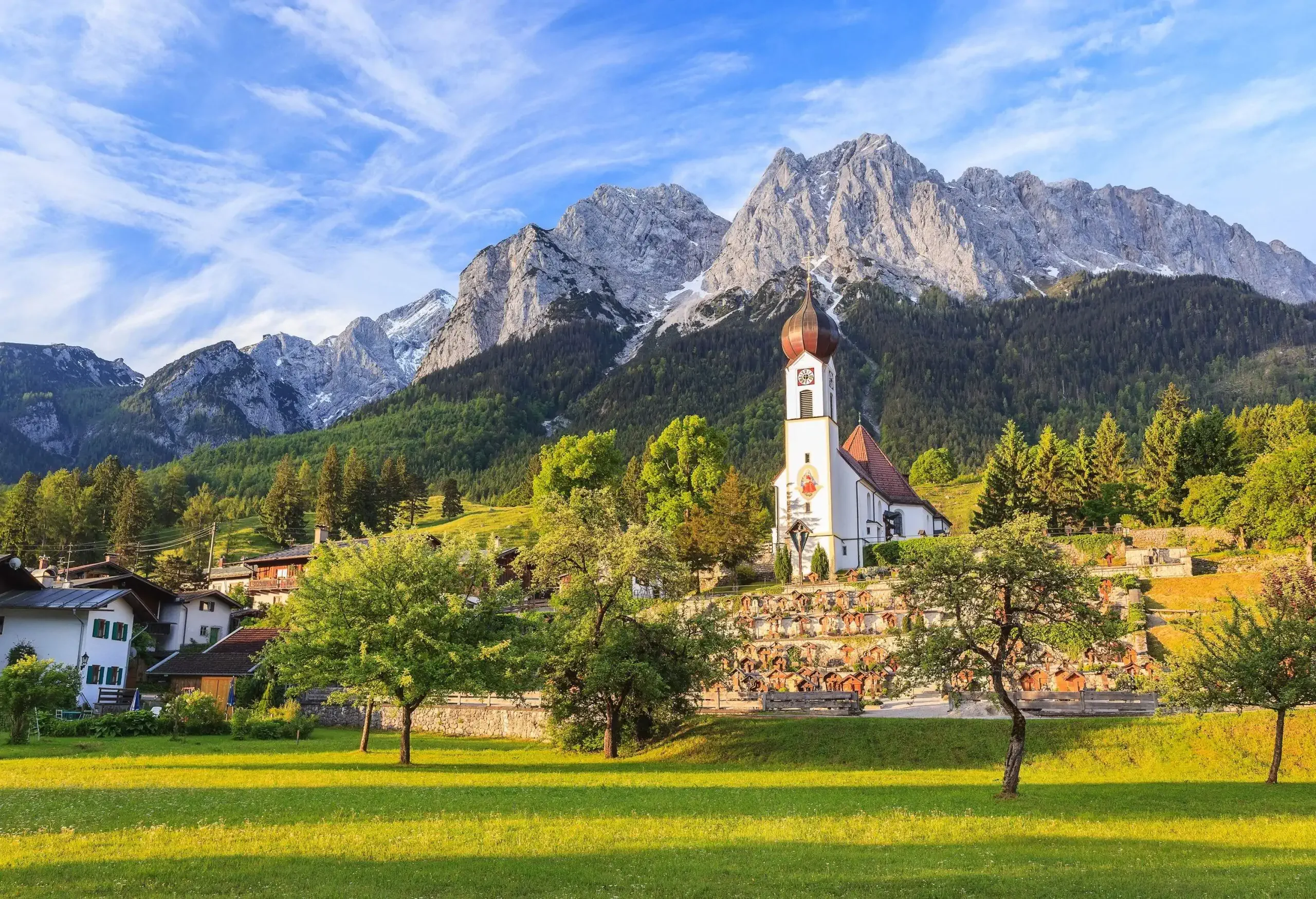 A white church with onion-shaped roof on a hill overlooking a green lawn with autumnal trees.
