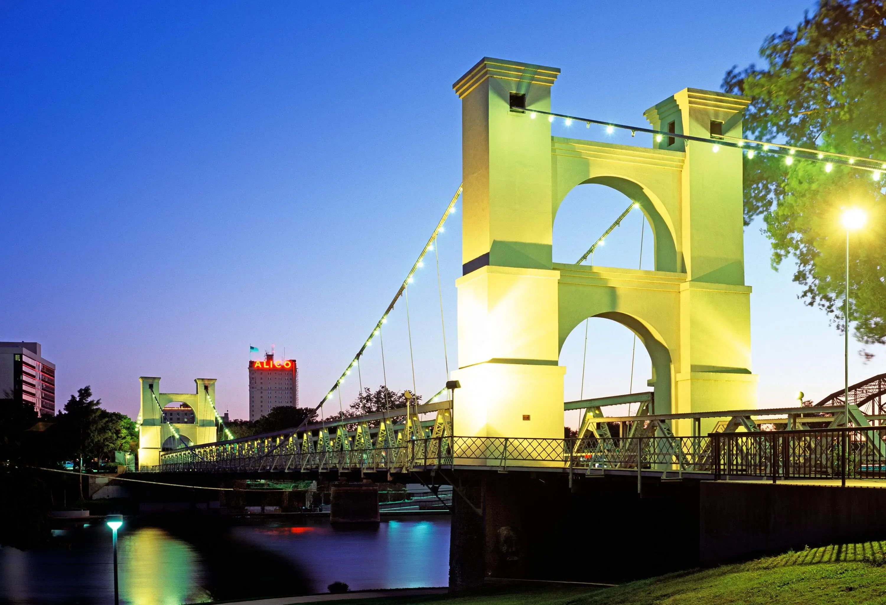 The majestic Waco Suspension Bridge, with its robust towers and intricate web of steel cables, gracefully spans the tranquil Brazos River.