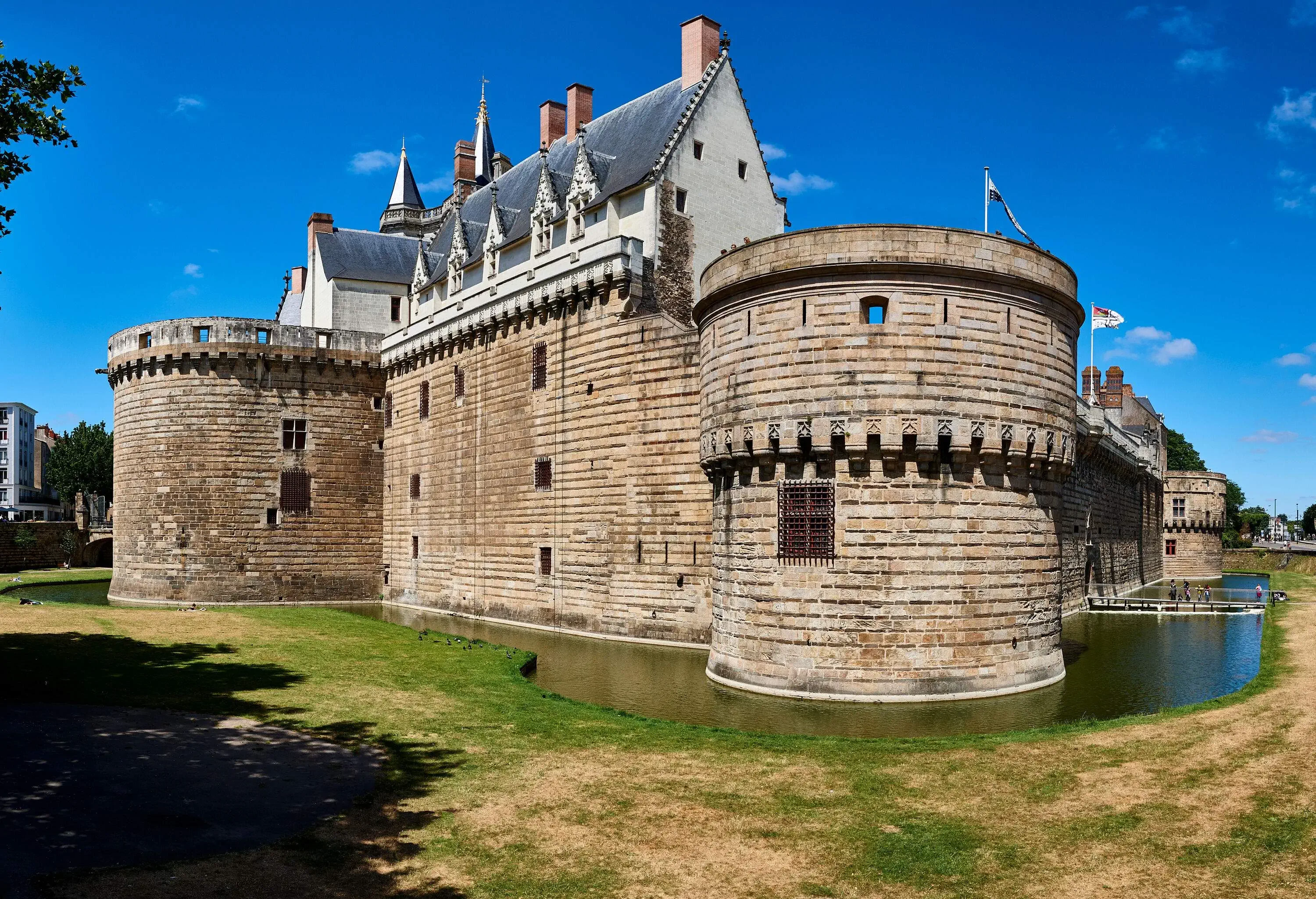 A historic castle with circular towers at each corner and a drawbridge for entrance, surrounded by a moat and grasslands.