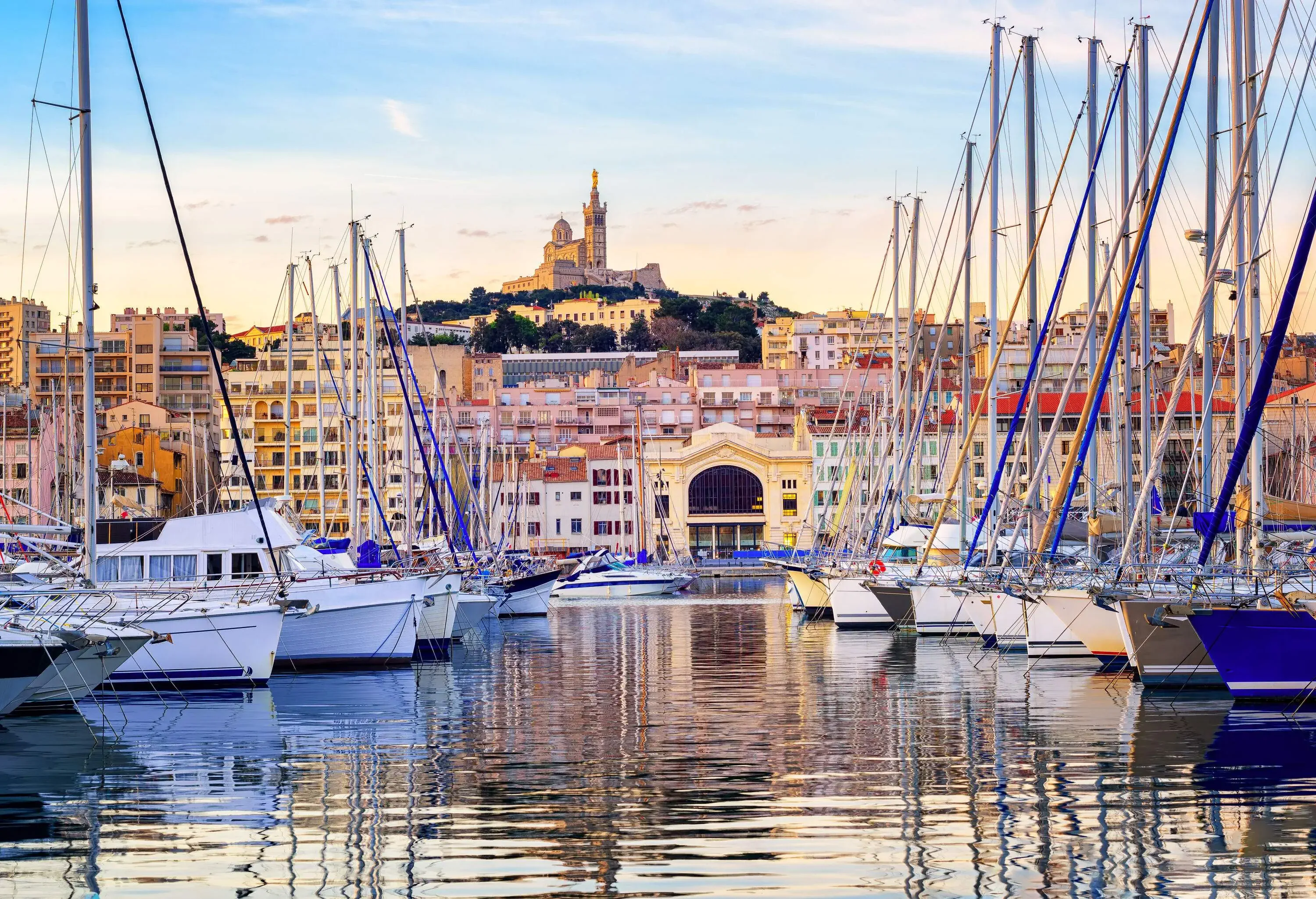 A harbour with docked boats with views of waterfront buildings and a hilltop church with a tower.